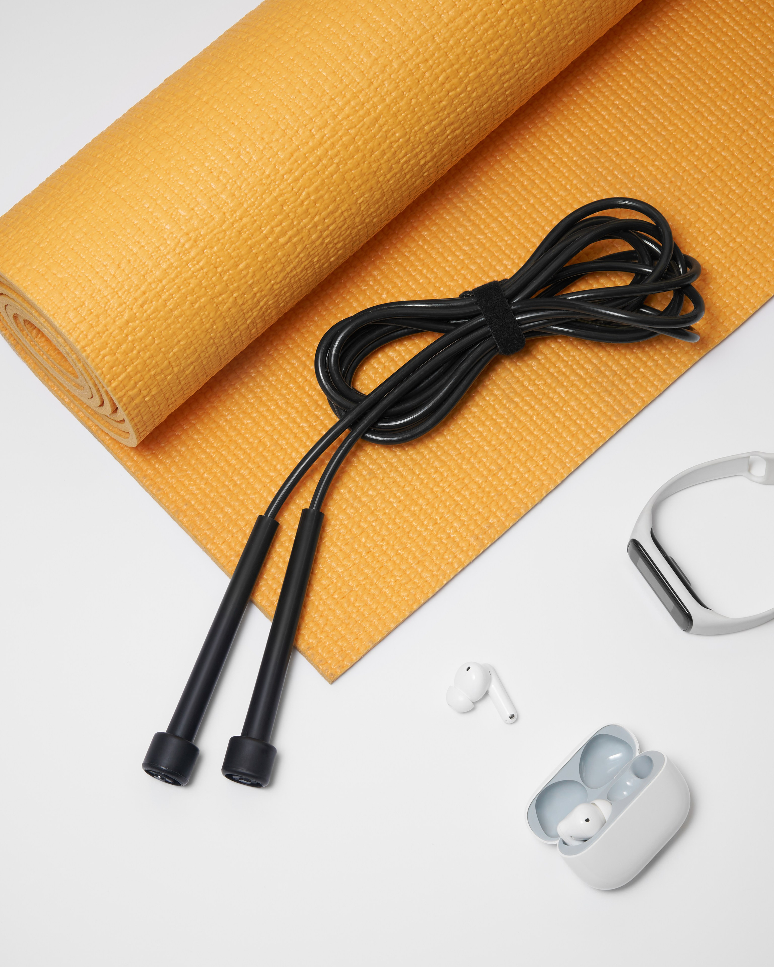 Черная скакалка лежит рядом с фитнес-принадлежностями на оранжевом коврике для йоги