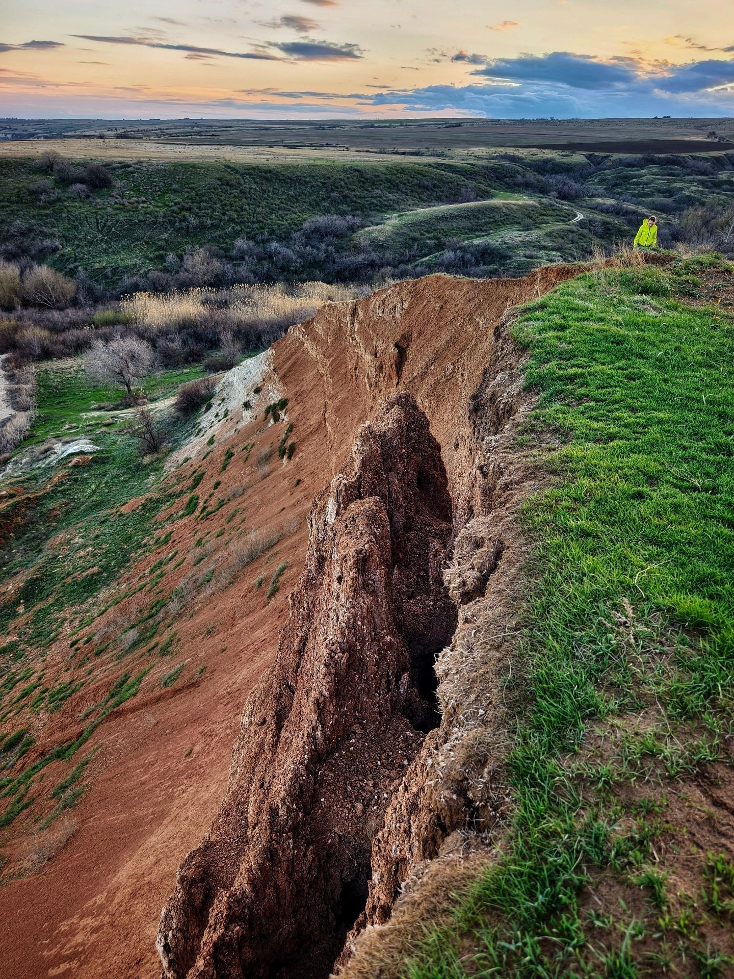 Глубокий овраг на фоне заката, с человеком в яркой одежде на краю
