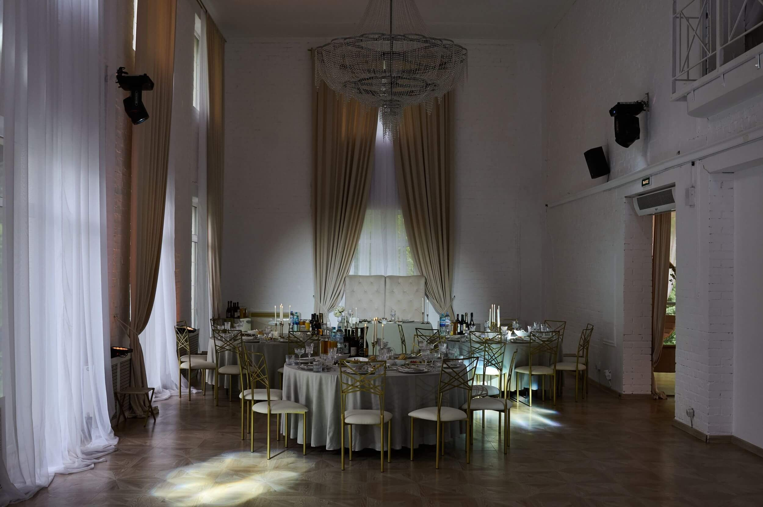 Интерьер банкетного зала Villa Park в Петергофе: просторные светлые помещения с высокими потолками и большими окнами. Элегантная мебель, стильные люстры и нейтральная цветовая гамма создают утончённую атмосферу для торжественного мероприятия.
