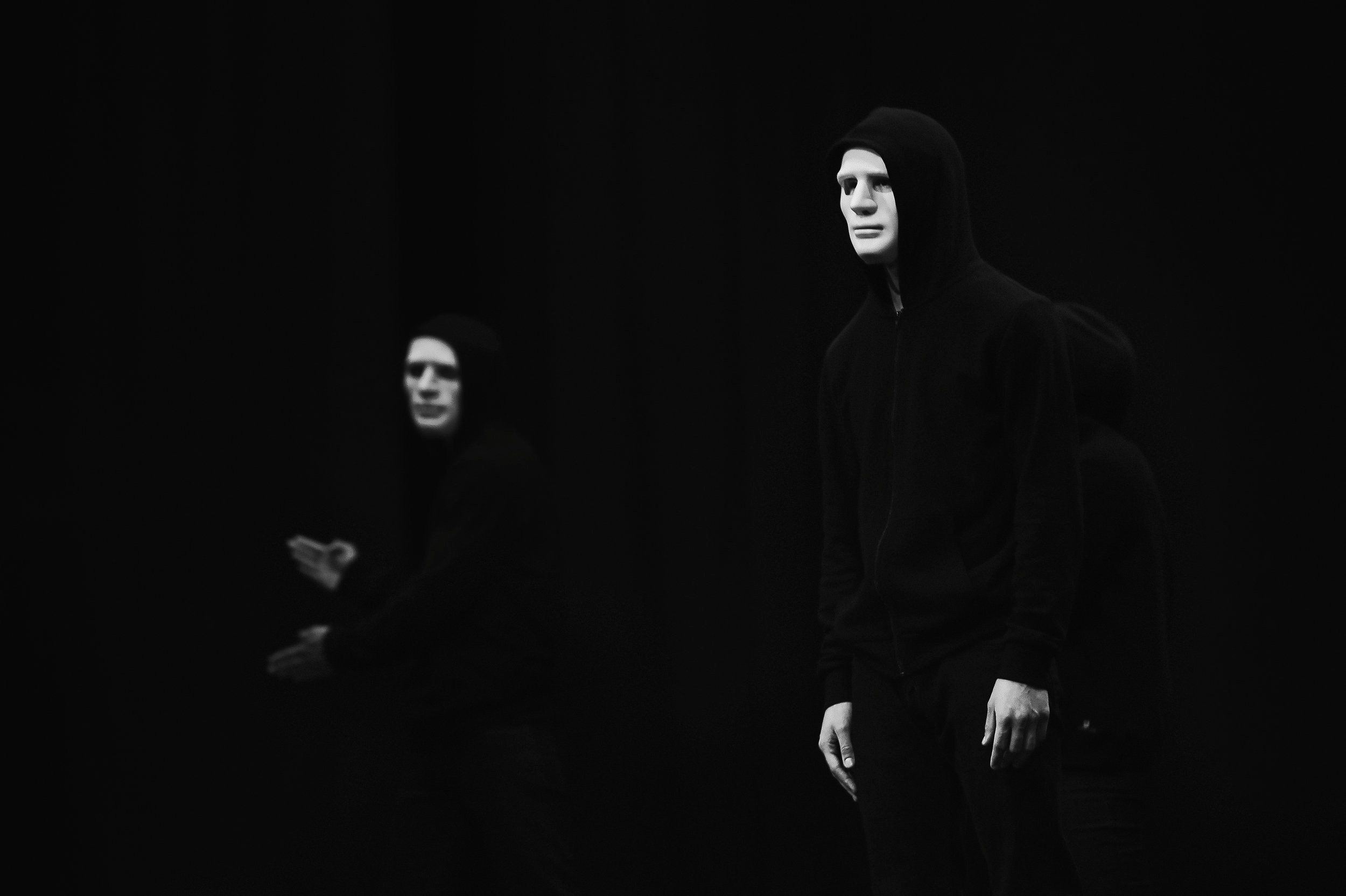 Актеры в белых масках и черных капюшонах на сцене, театральное фото