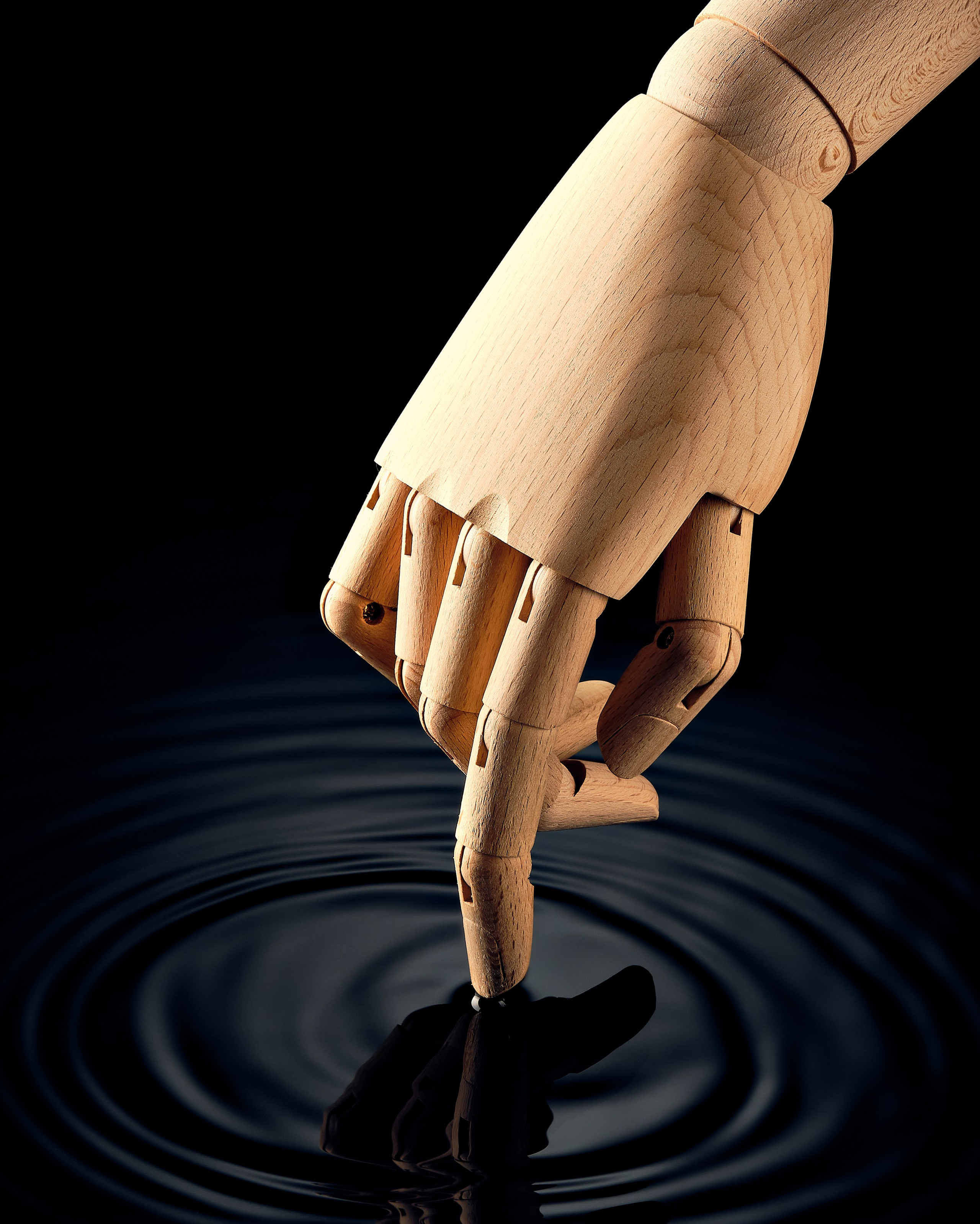 Деревянная манекенная рука касается чёрной воды, создавая концентрические круги.