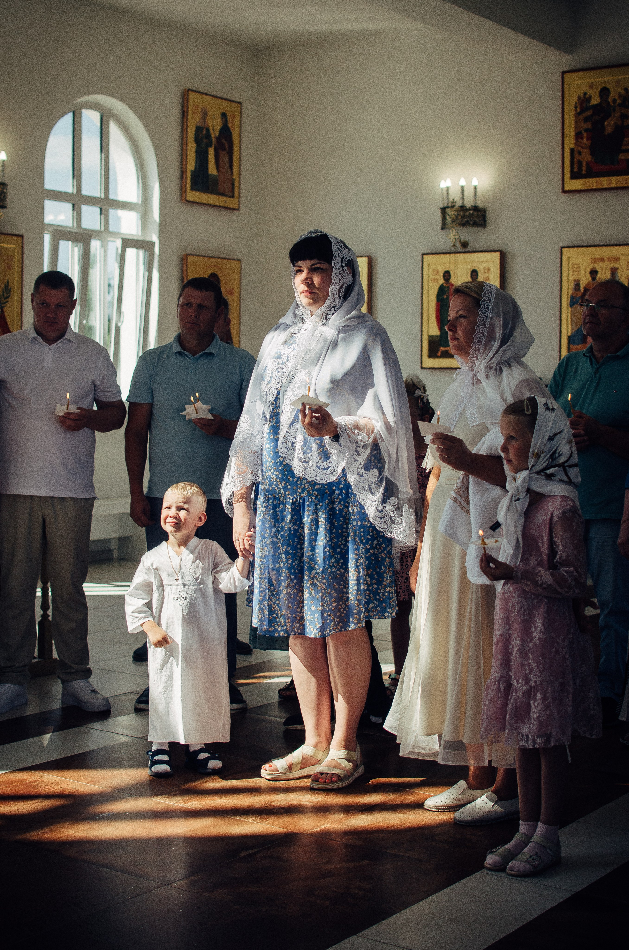 Мама с сыном стоит у алтаря в церкви во время таинства крещения.