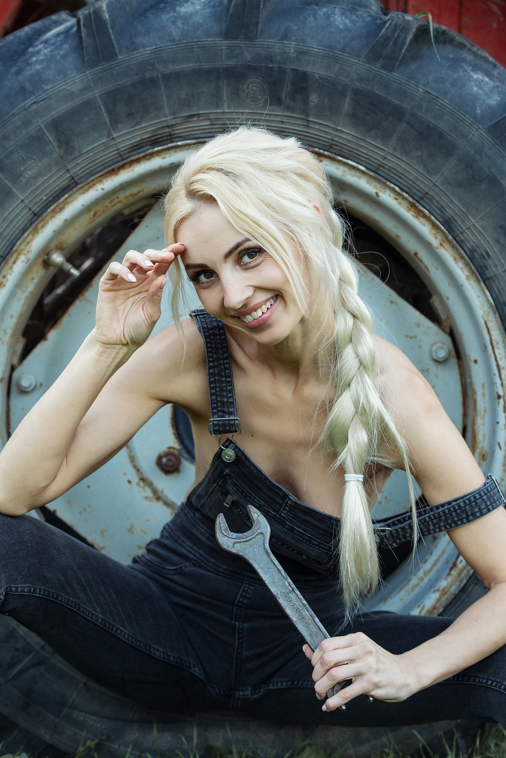 блондинка с гаечным ключом у колеса трактора сидит улыбаетсяидит