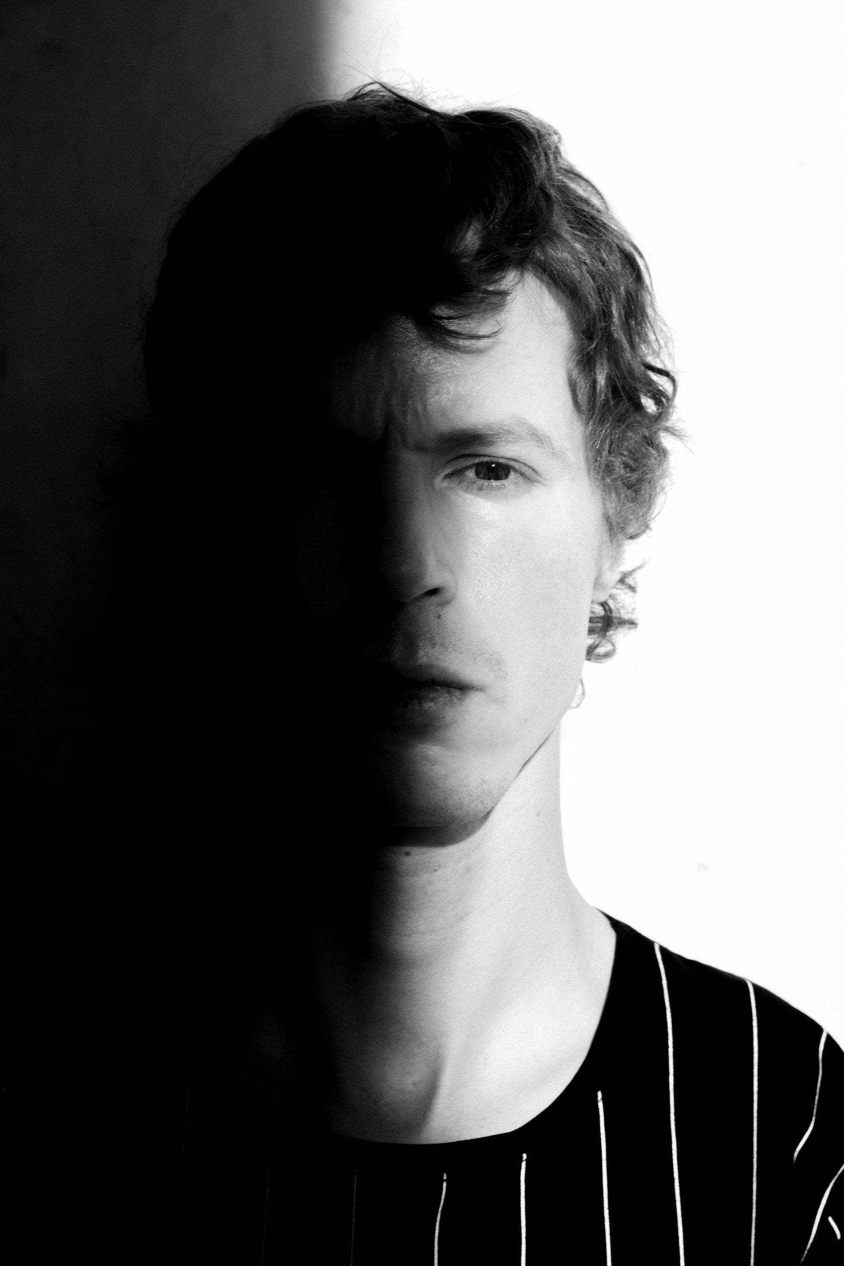 Close-up black and white portrait of a man from the shoulders up in a black t-shirt, contrasting light and shadow on the face