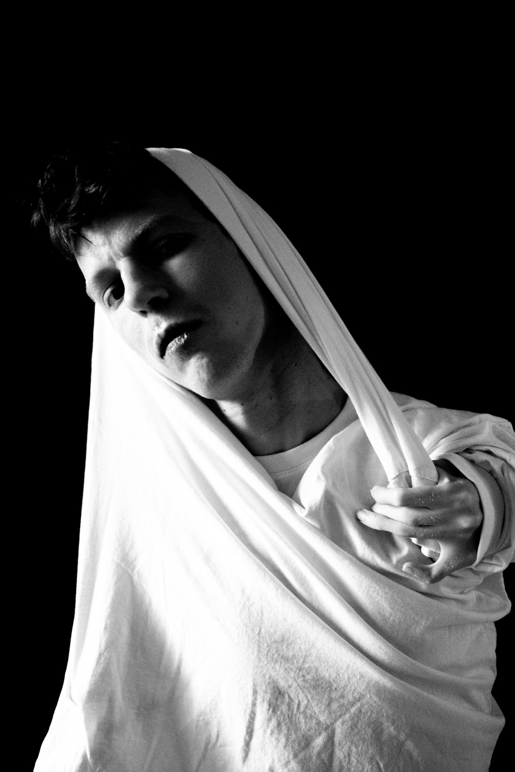 Conceptual black and white portrait of a man in a white sweater, gaze directed into the camera