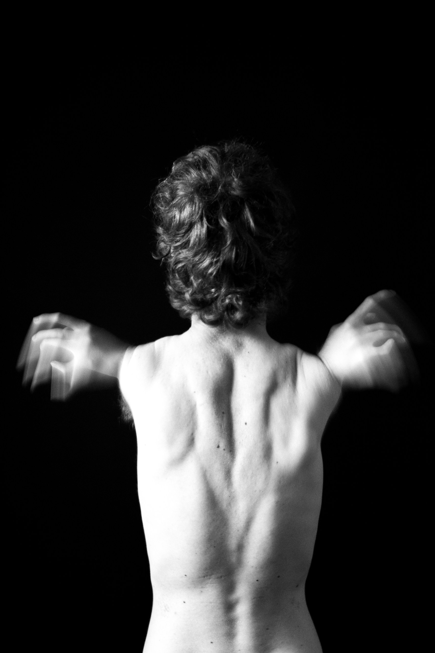 Artistic black and white photo of a man from the back, fluid movement of arms resembling wings