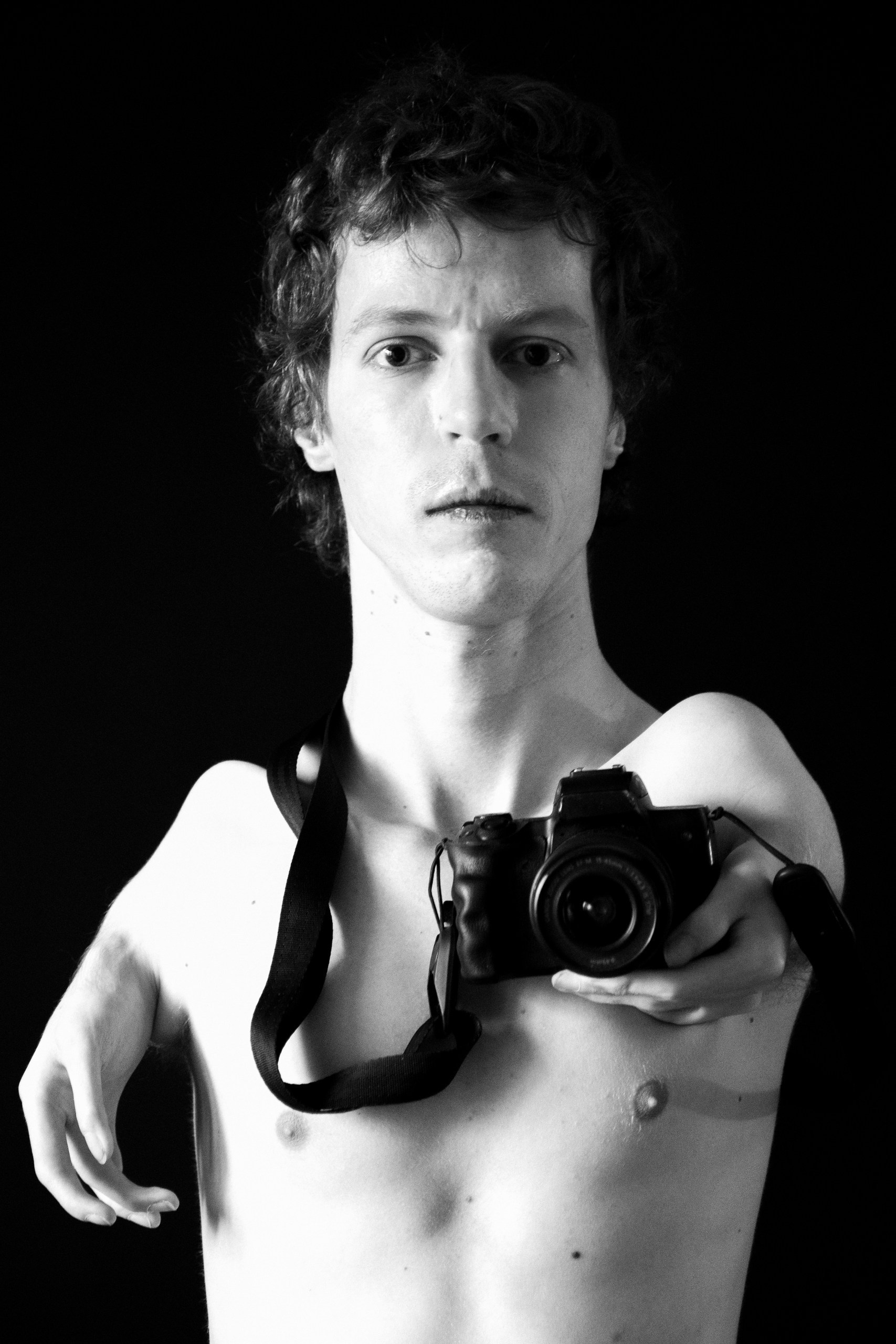 Strict black and white psychological portrait of a photographer with a camera in his hands on a black background