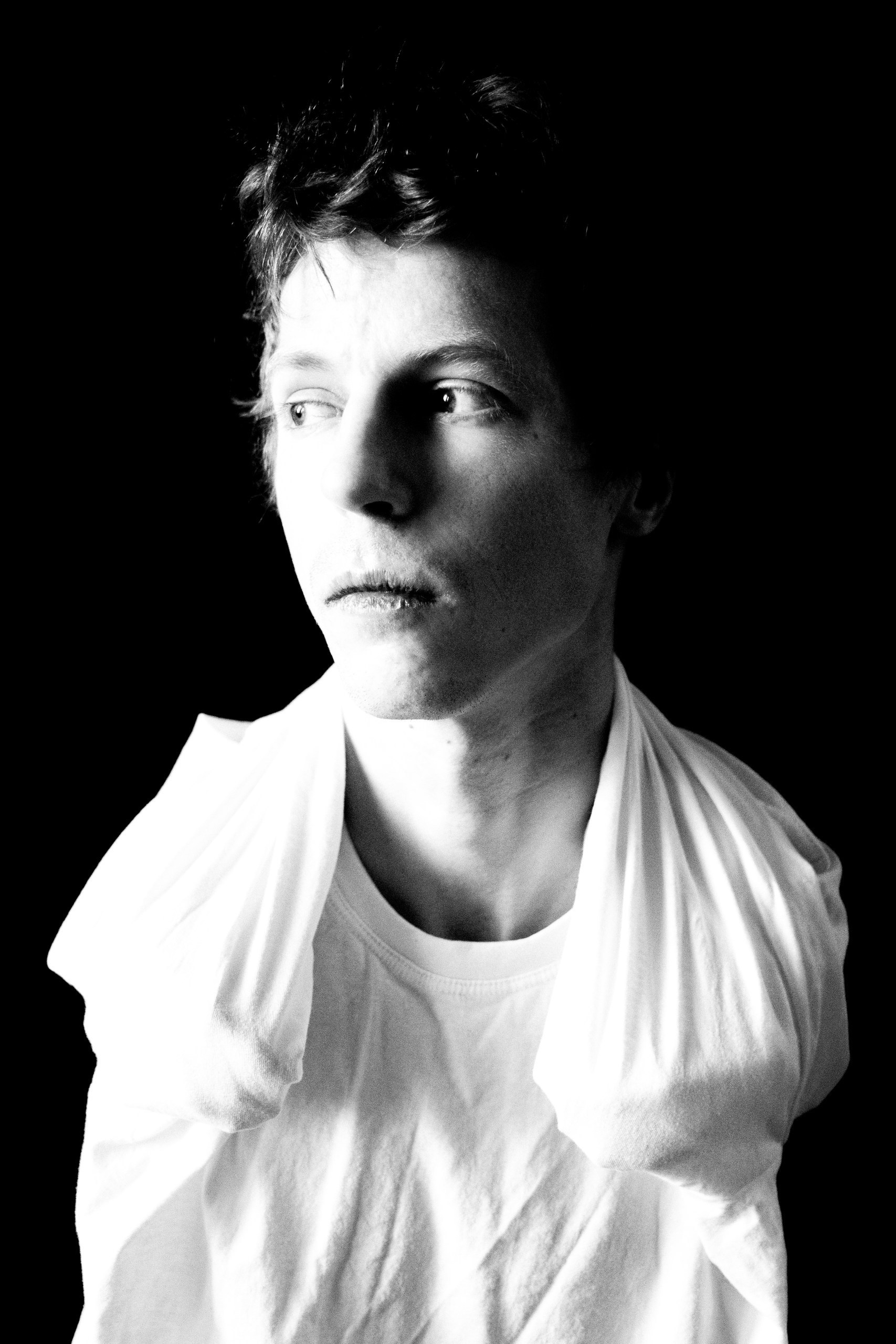 Monochrome art portrait of a man in a white sweater on a black background, looking away