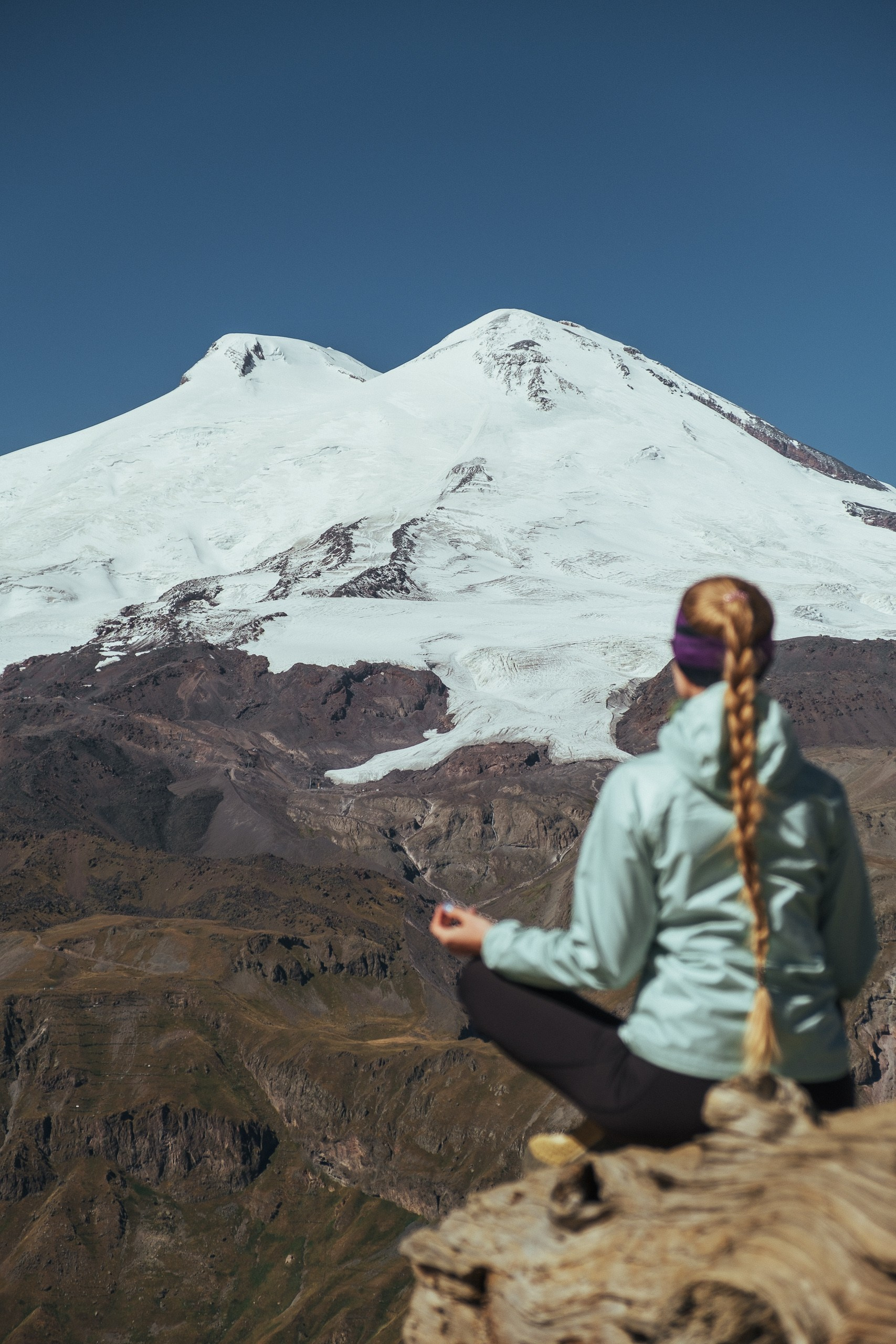 Девушка медитирует на горном хребте на фоне Эльбруса, вид на вершину