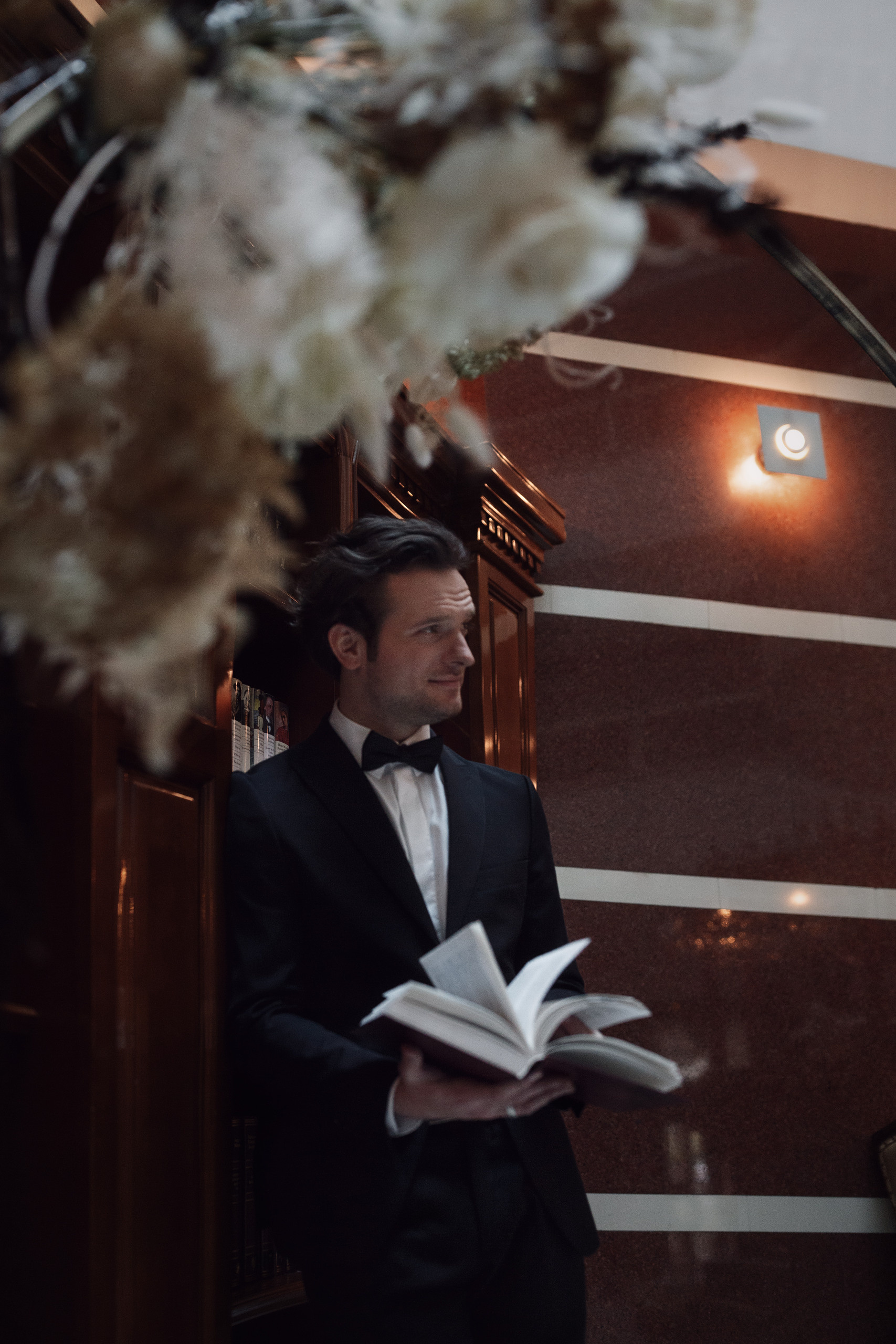 Жених модельной внешности стоя у полки с книгами листает одну из книг.