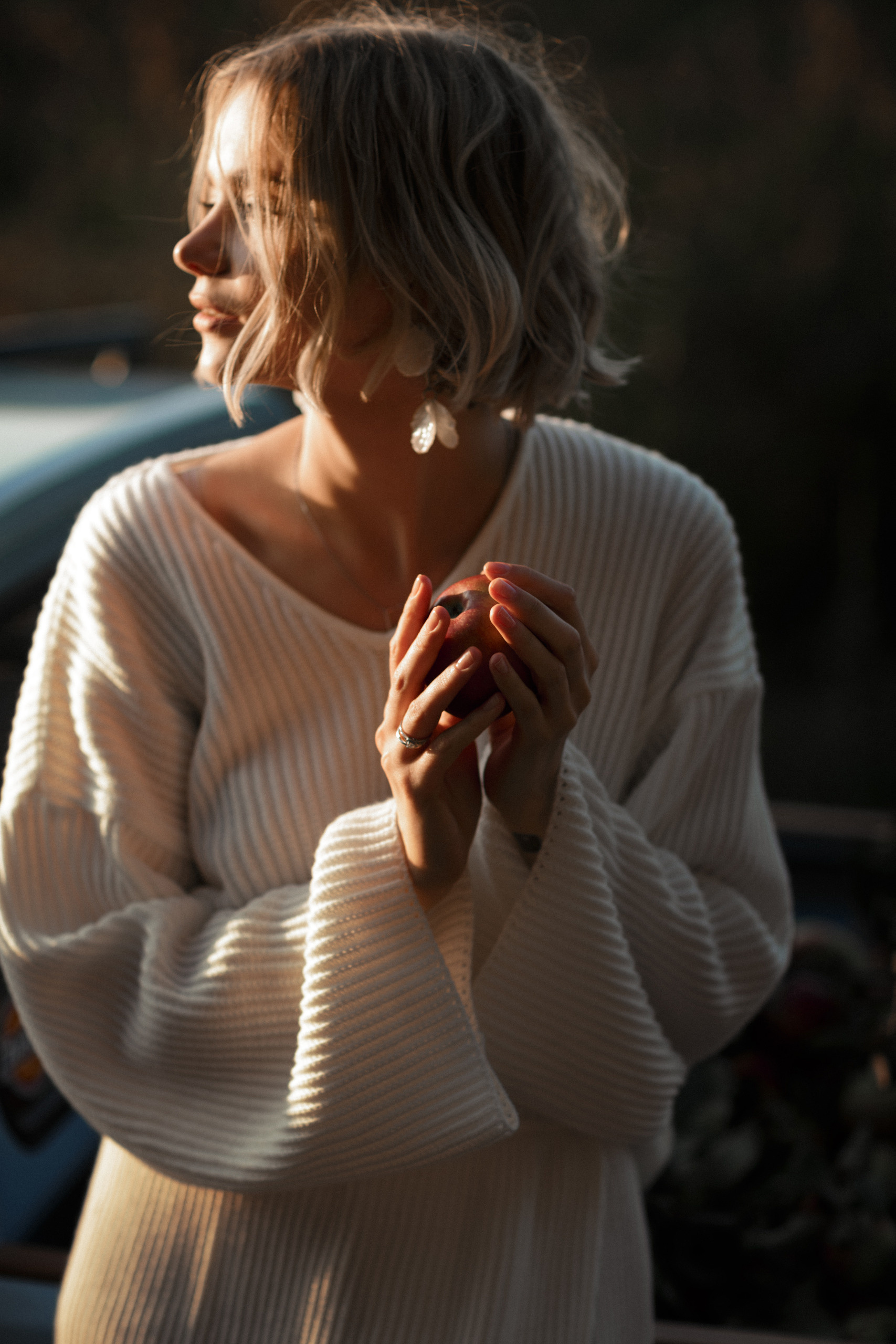 Высокая невеста в белом платье держит яблоко в руках, смотря на своего уже мужа.