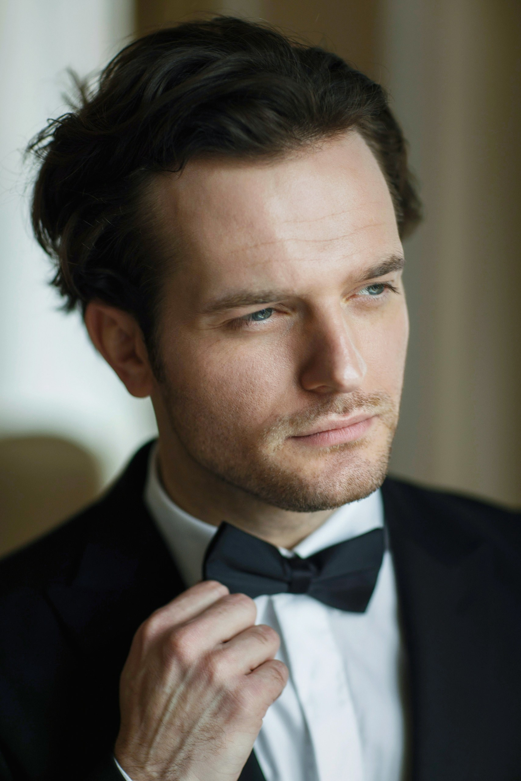 Стильный потрет очень красивого жениха в белой рубашке, черной пиджаке, черной бабочкой.