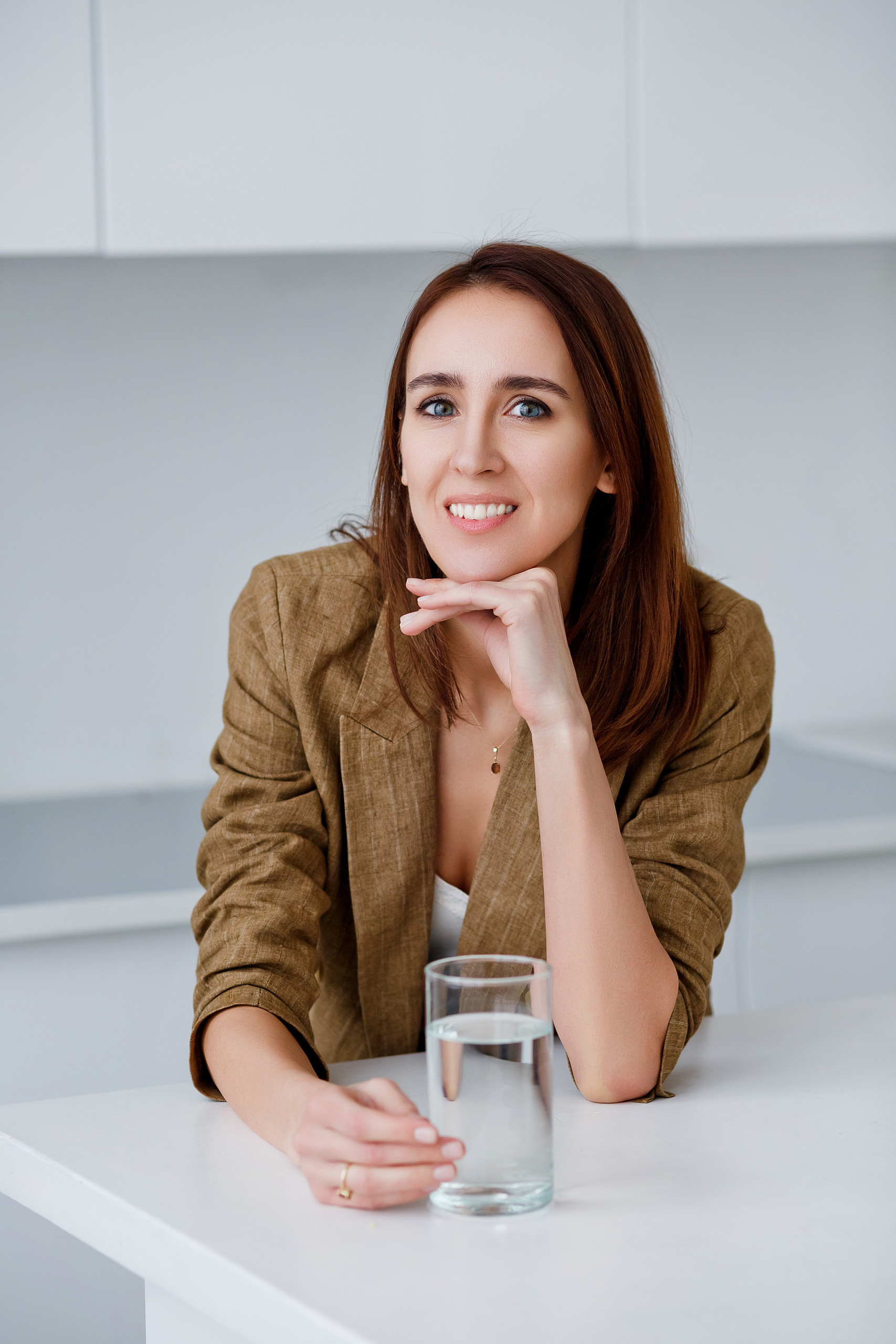 Девушка нутрициолог в льняном пиджаке на фоне светлой кухне с стаканом чистой воды 