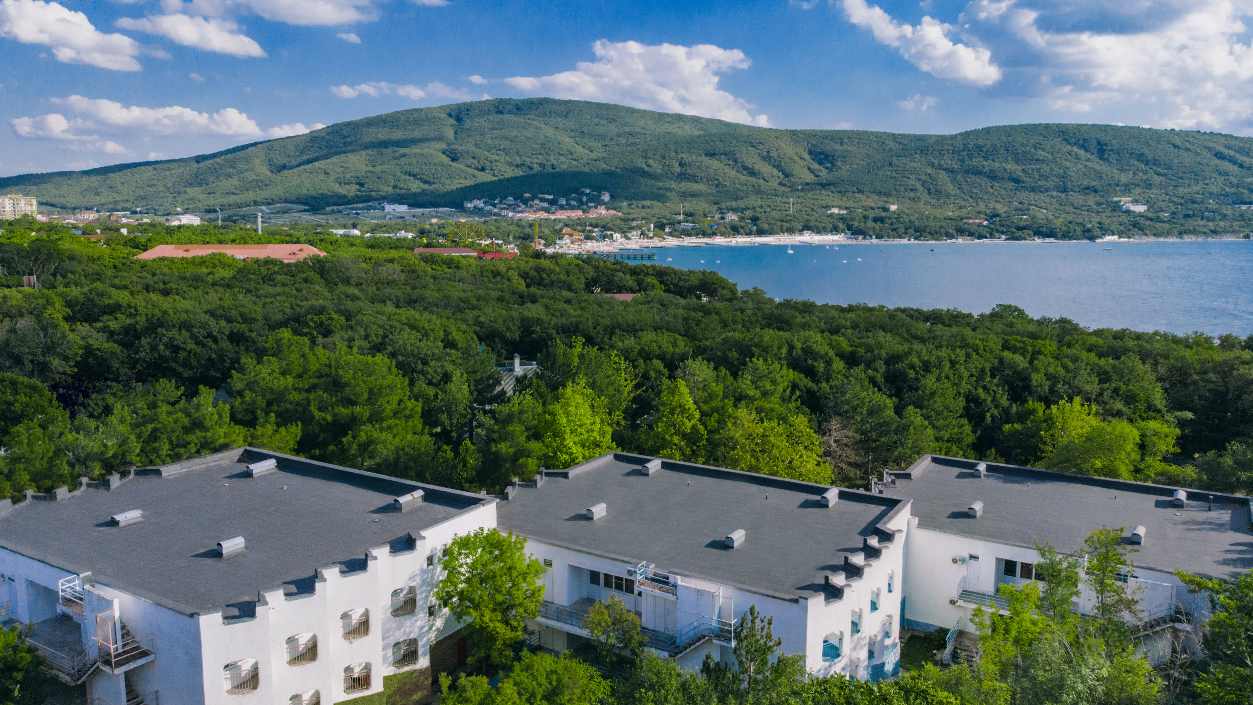 Зеленые горы вдали, синее море, жилые корпуса "Бригантина", "Каравелла", "Фрегат", вид с воздуха на лагерь Альбатрос