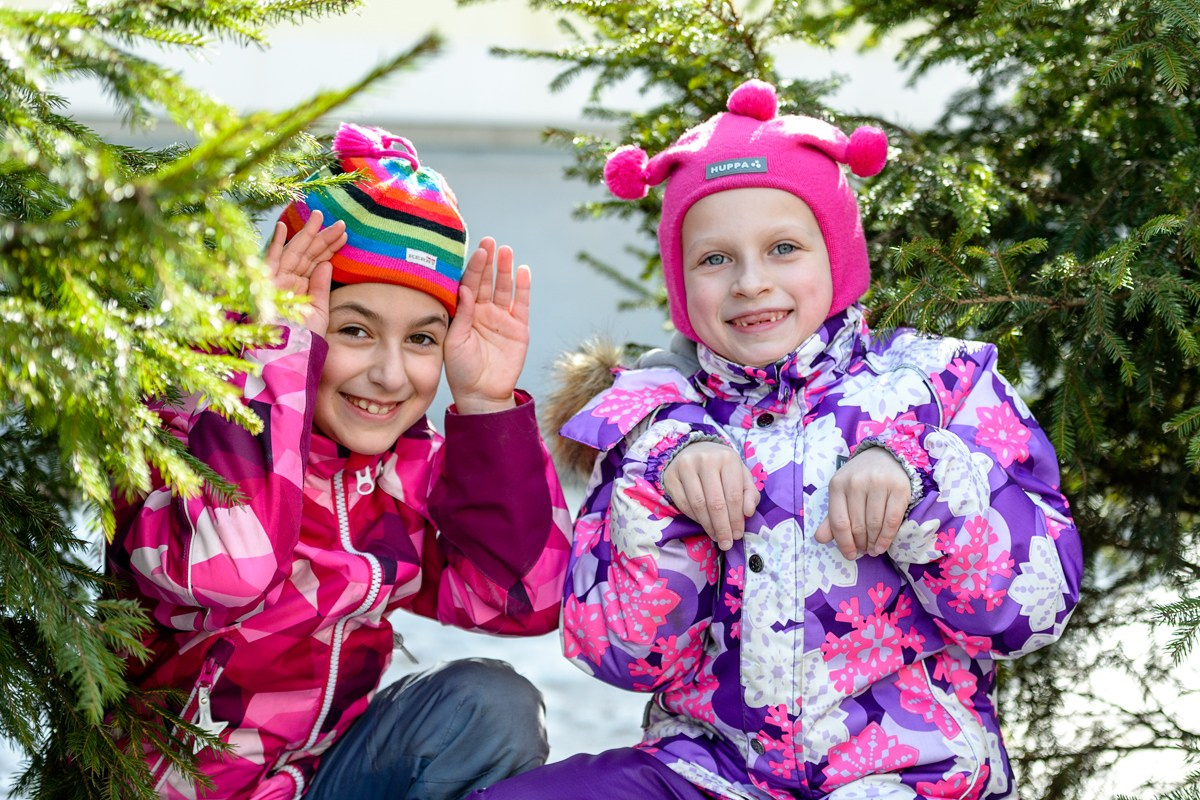 две девочки в яркой теплой одежде на прогулке прячутся за ёлками
