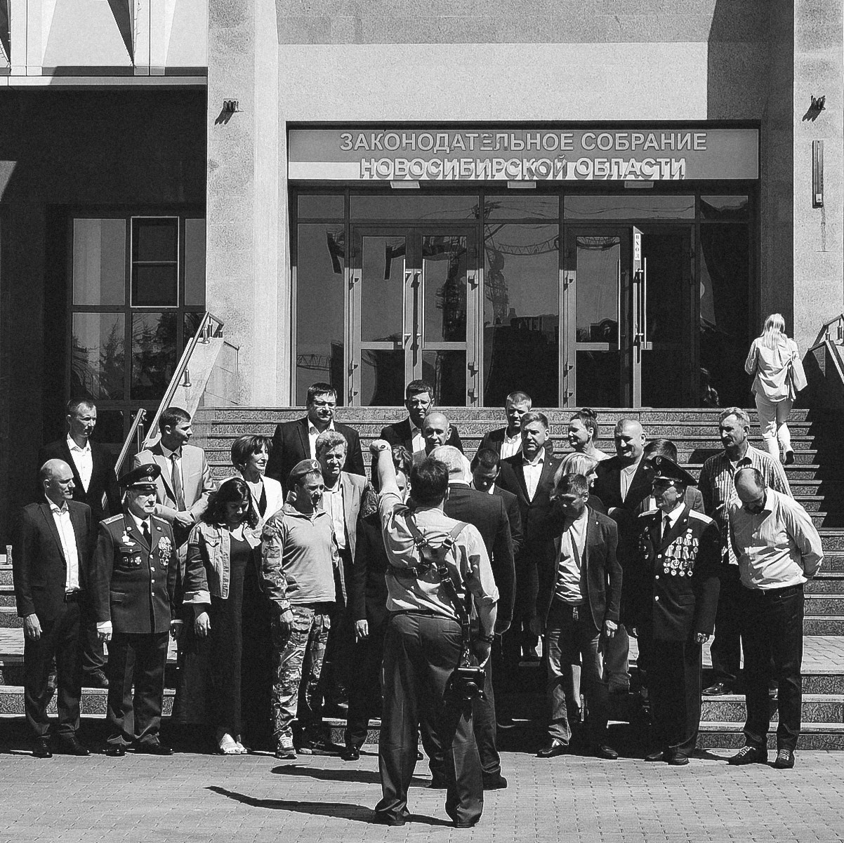 Фотограф Василий Дан руководит процессом коллективной съемки депутатов и военных на крыльце Законодательного собрания Новосибирской области. Репортажная черно-белая фотография, бэкстейдж.