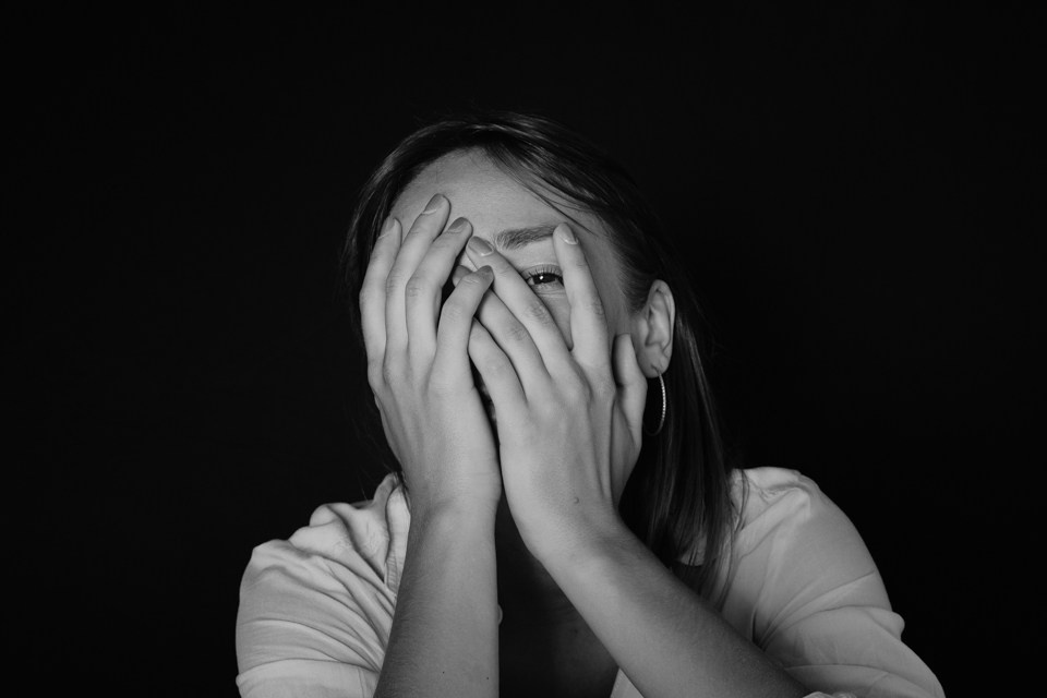 Фотоснимок девушки закрывавший лицо руками на черной фоне