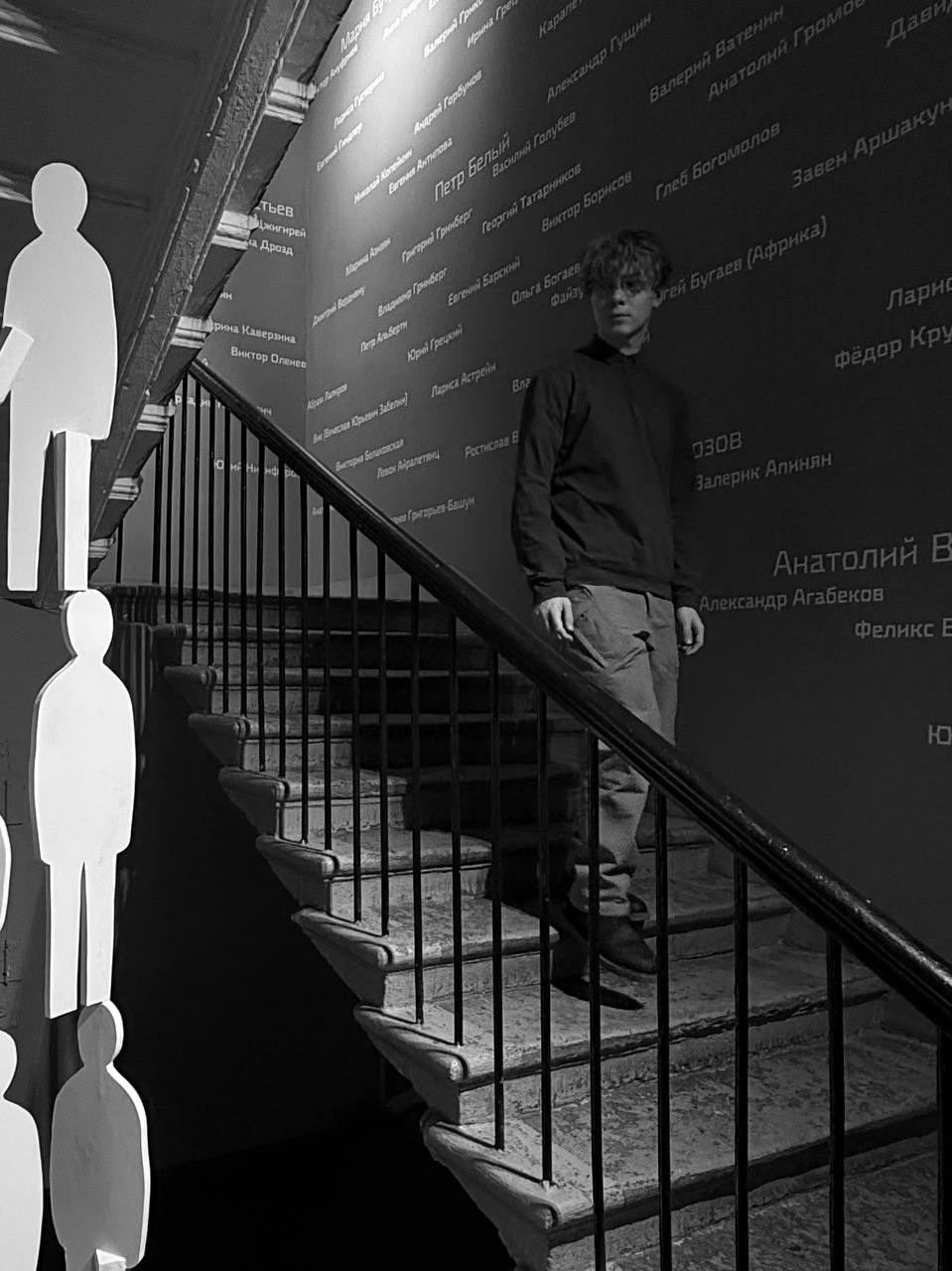 молодой человек с кудрявыми волосами на лестнице креативного музея в Санкт-Петербурге, чёрно-белая художественная фотография с архитектурной композицией