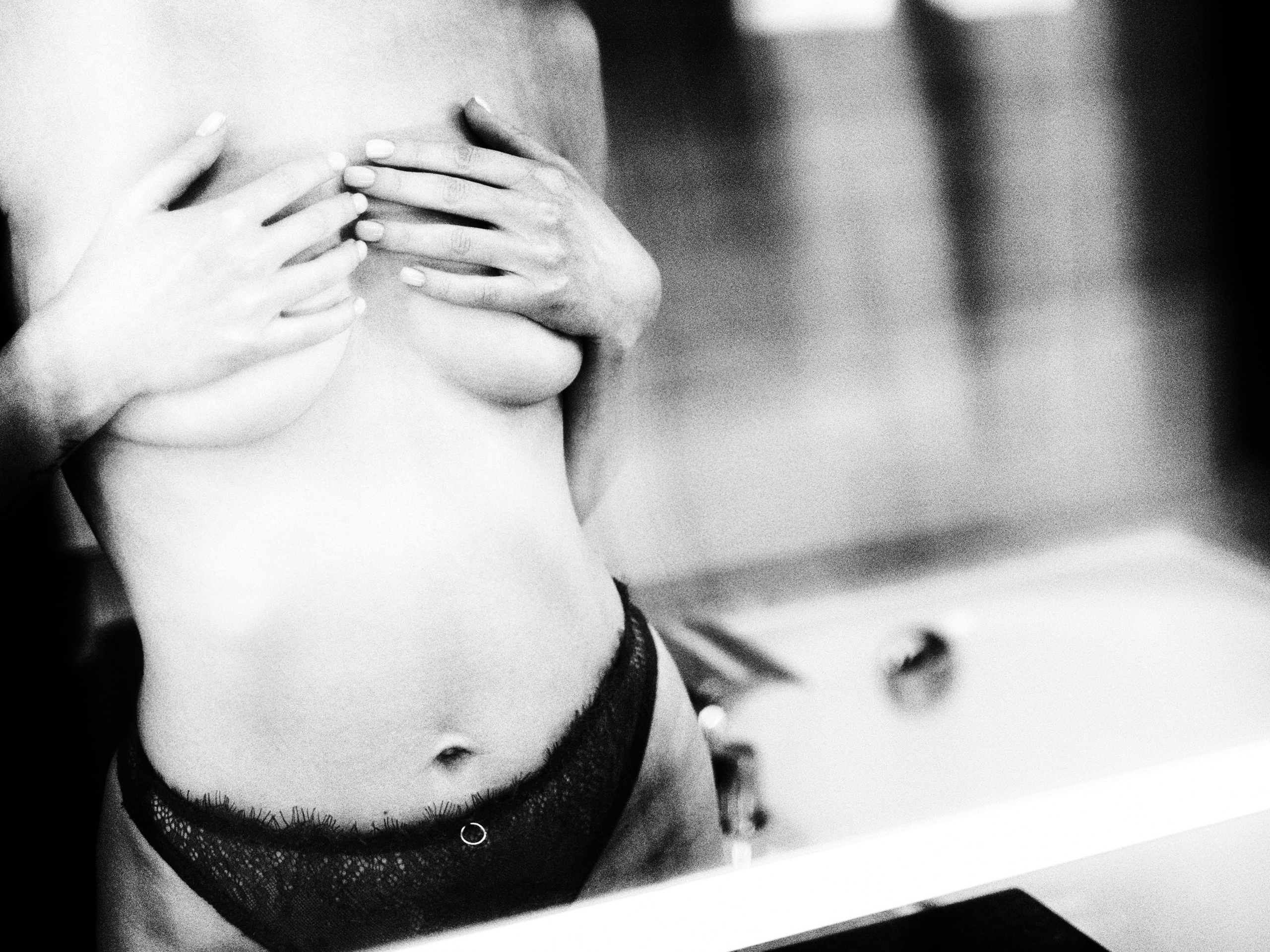 Женщина стыдливо прикрывает небольшую грудь руками перед зеркалом.