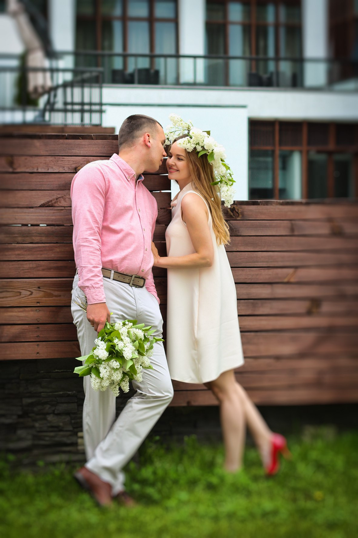 мужчина с букетом сирене целует девушку в коротком платье и венке