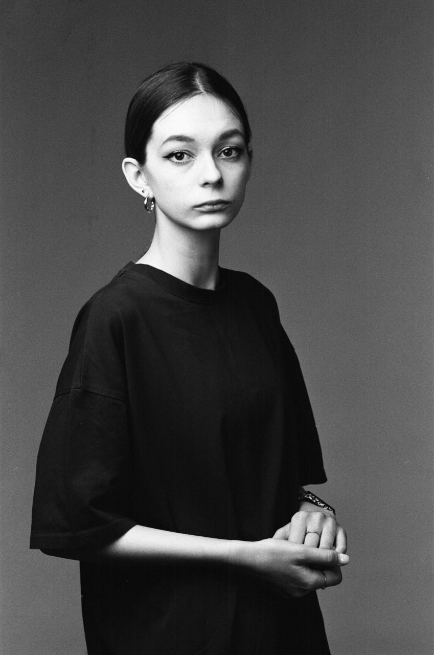 Девушка в темной одежде на нейтральном фоне, черно-белый пленочный портрет.