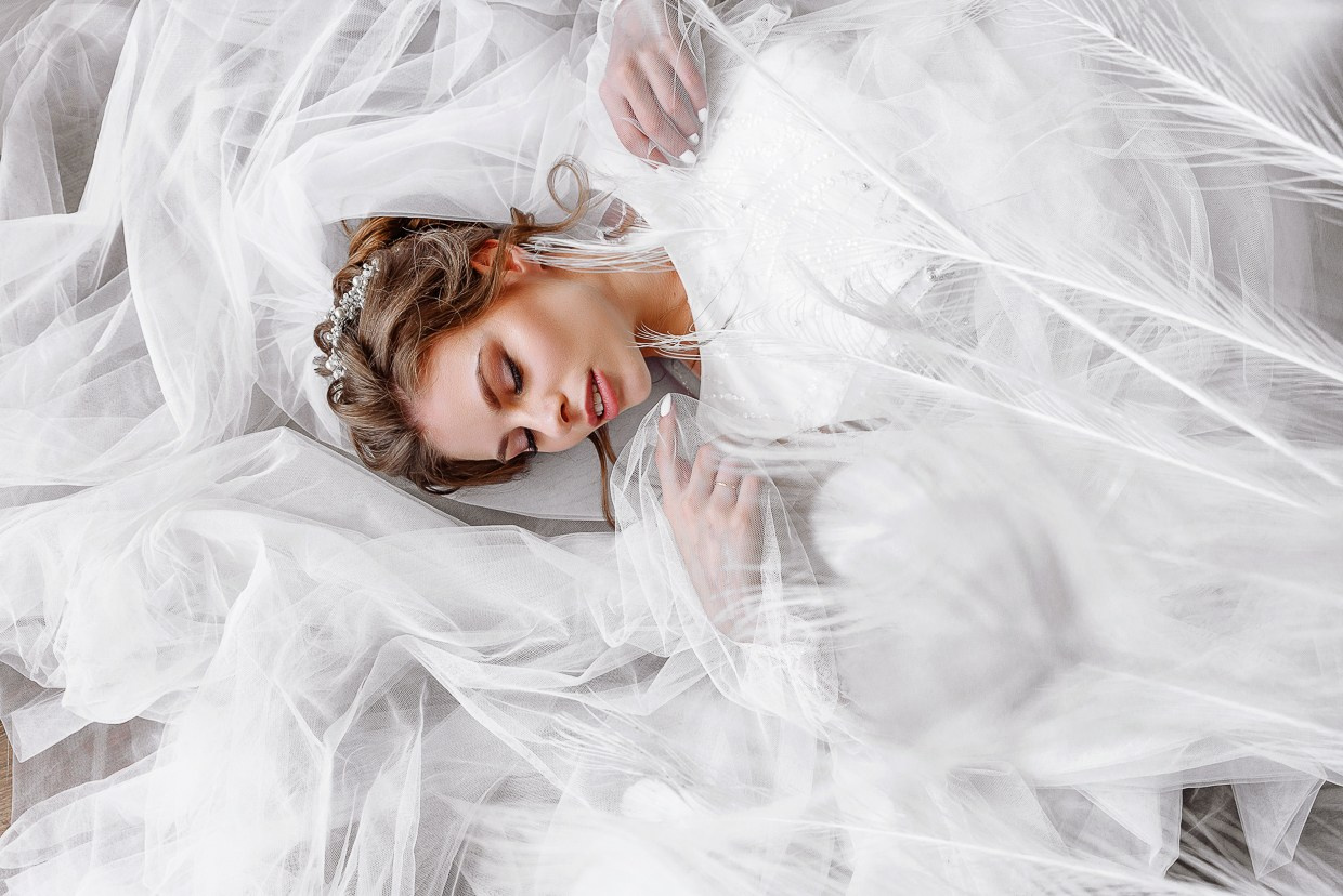 невеста в фате лежит на полу под перьями