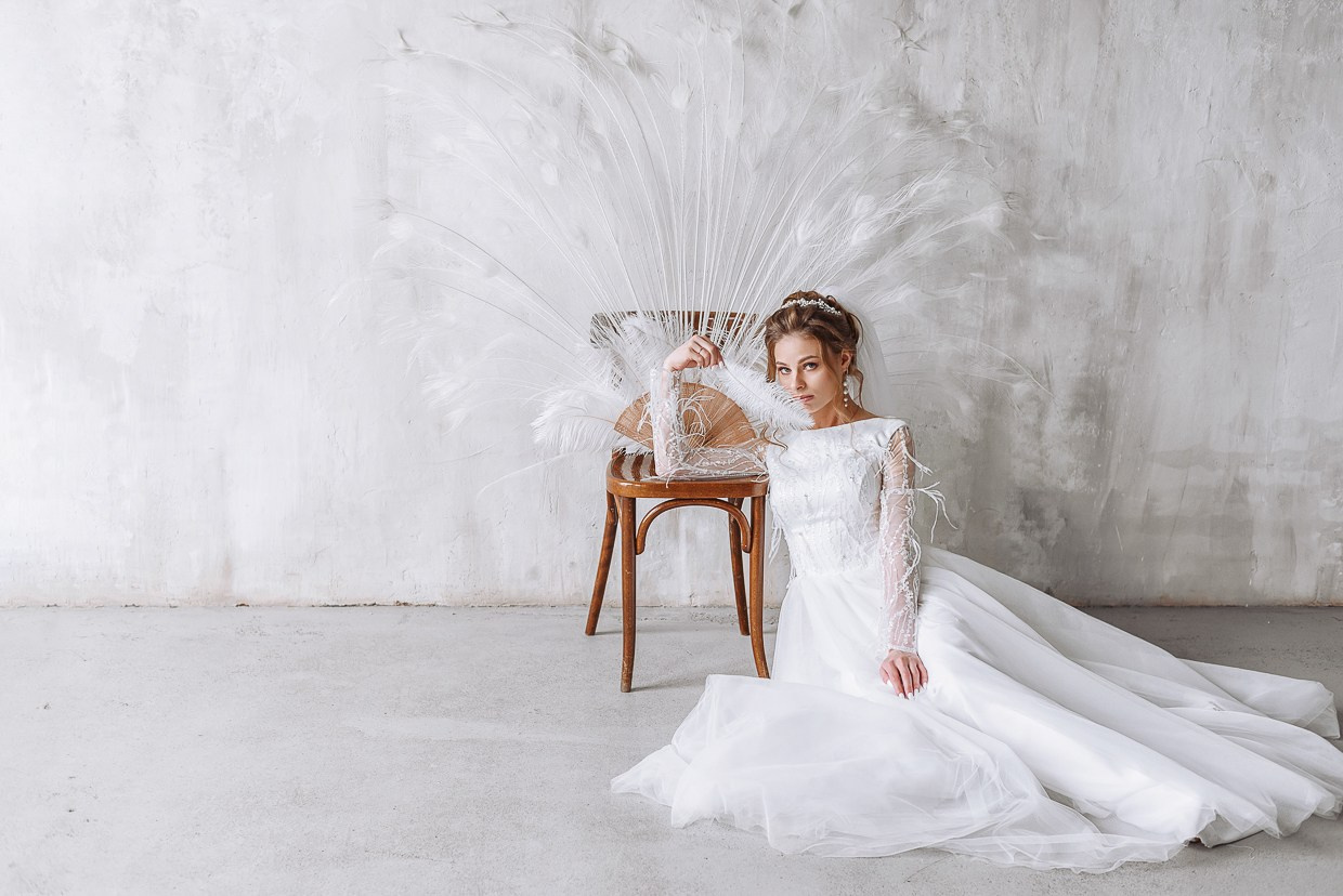 невеста сидит на полу с белыми перьями павлина