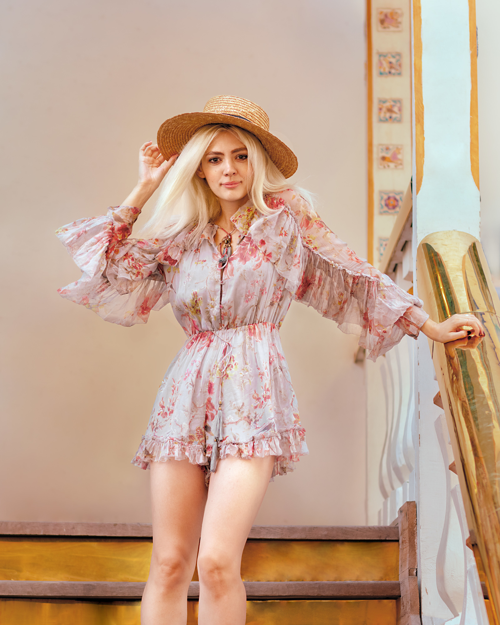 Девушка в легком, летнем платье придерживая рукой шляпку спускается с лестницы