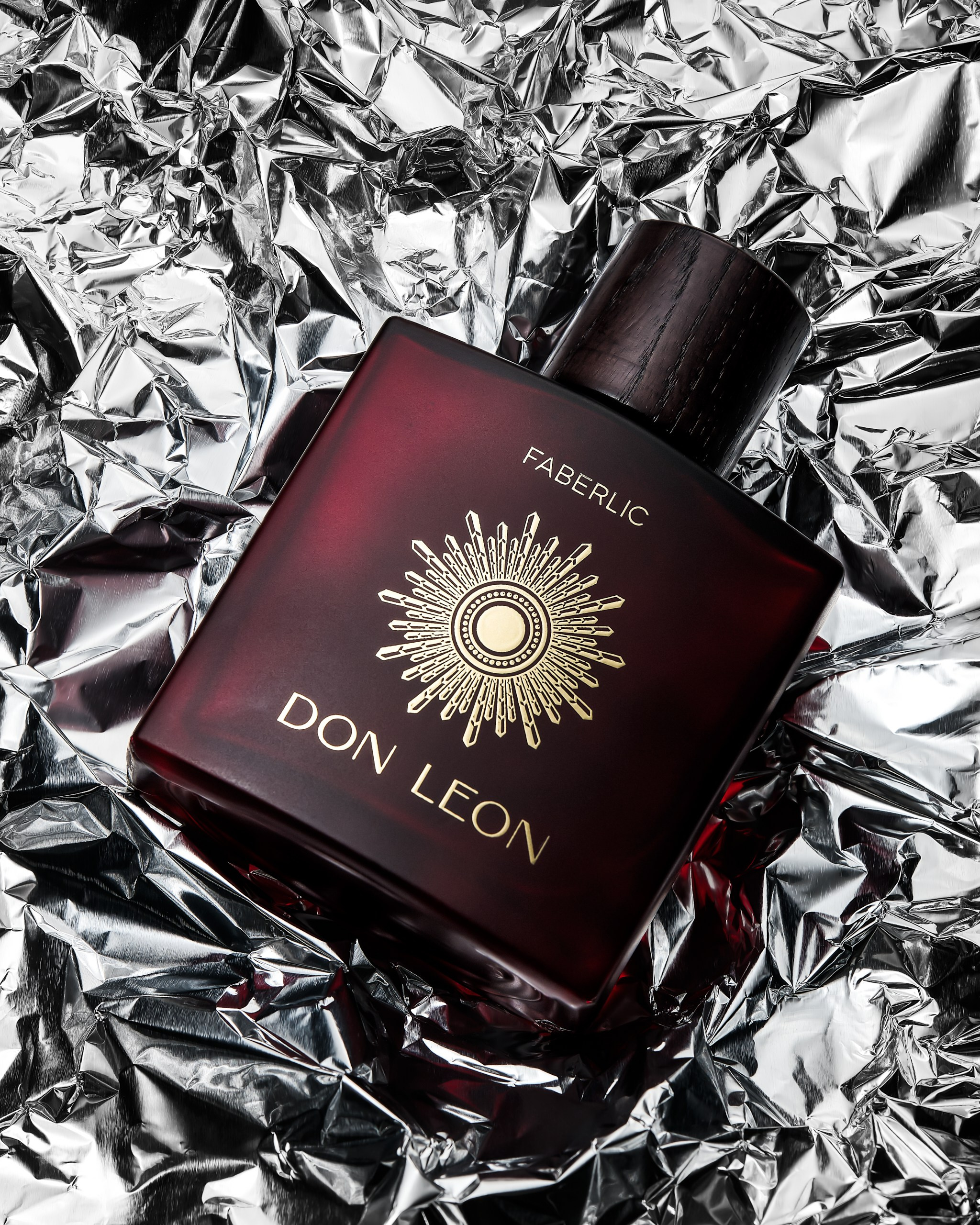 Бутылка одеколона Don Leon на смятой фольге с контрастными отражениями и подсвеченным логотипом.