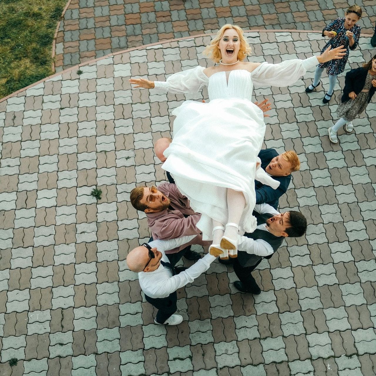 Друзья жениха подбрасывают невесту вверх. Невеста в белом платье кричит от эмоций