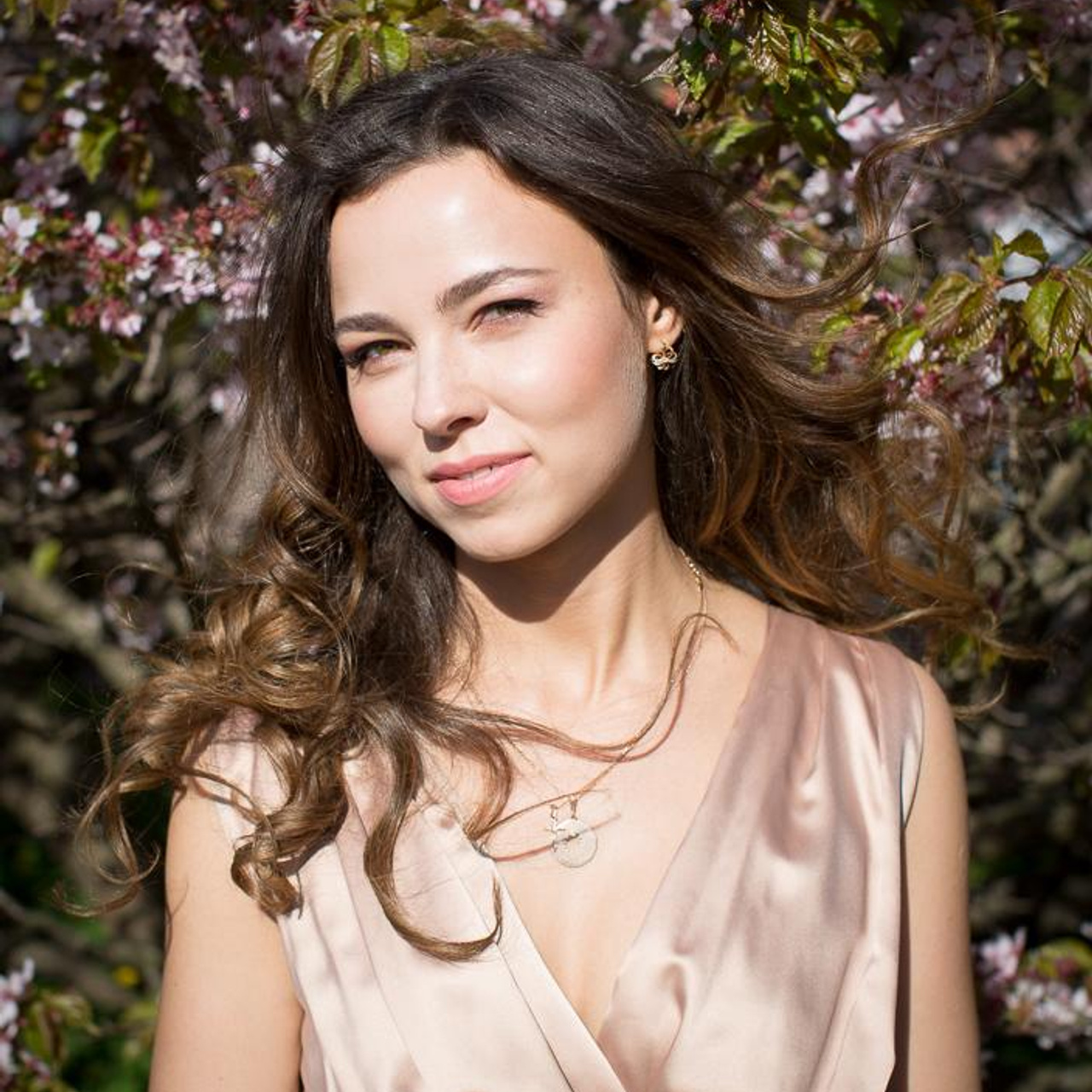 Прекрасная девушка брюнетка на фотосессии в цветущей сакуре в ботаническом саду, ее волнистые волосы развеваются от ветра