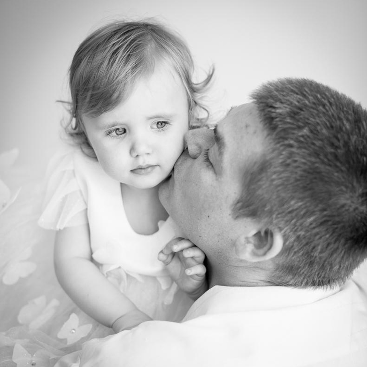 Фотосессия в черно белом стиле маленькой принцессы в пышной юбке и перьях, папа целует ее в щеку и смотрит с обожанием