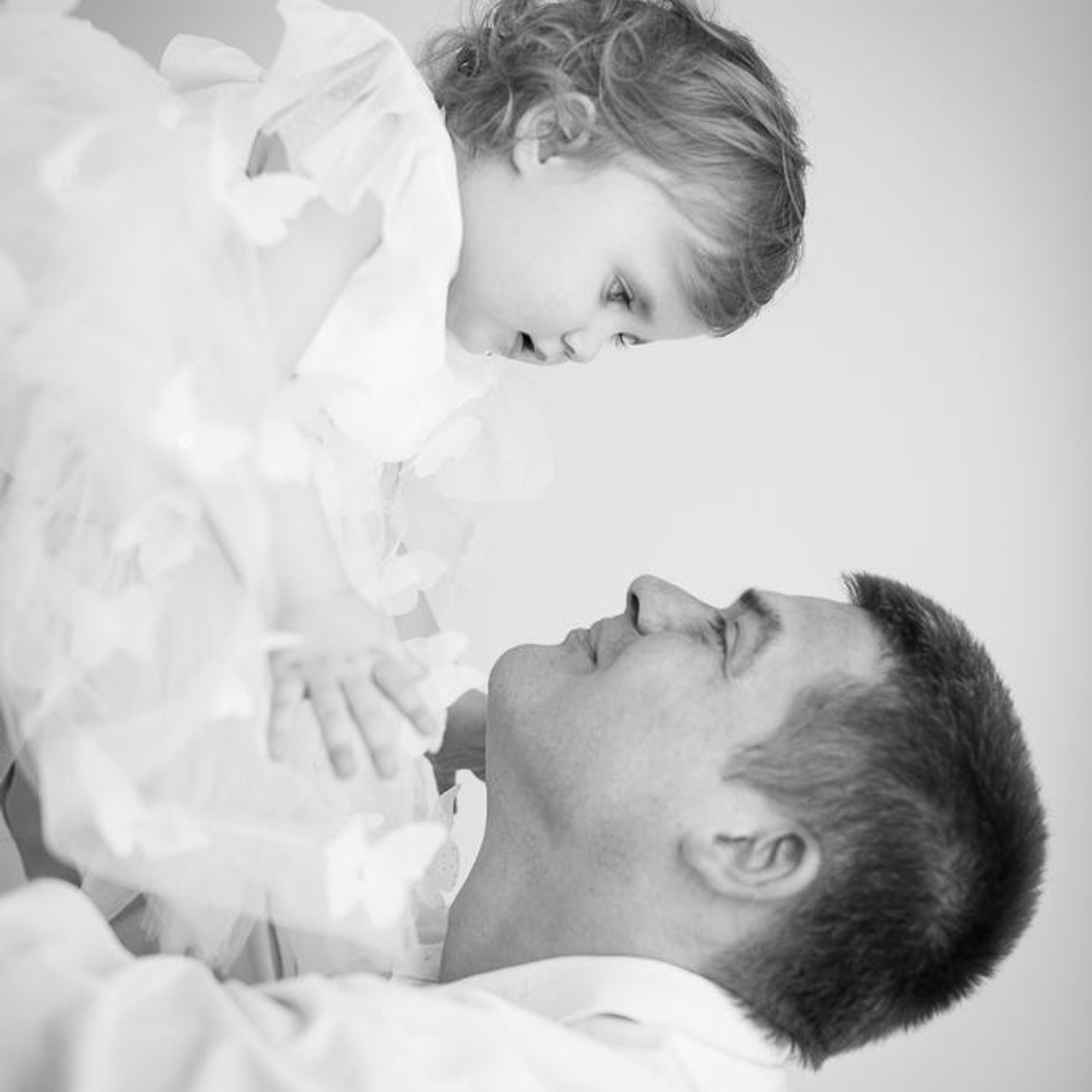 Фотосессия в черно белом стиле маленькой принцессы в пышной юбке и перьях, папа держит ее на руках и смотрит с обожанием