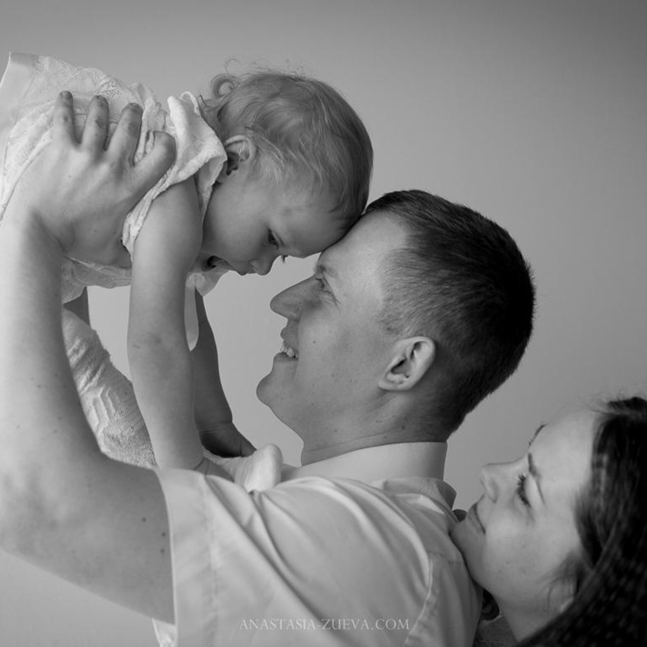 Семейная фотосъемка в домашней фотостудии в приморском районе Санкт-Петербурга, мама  папа и маленькая дочка на руках у папы, ощущение единения счастья и умиления после съемки