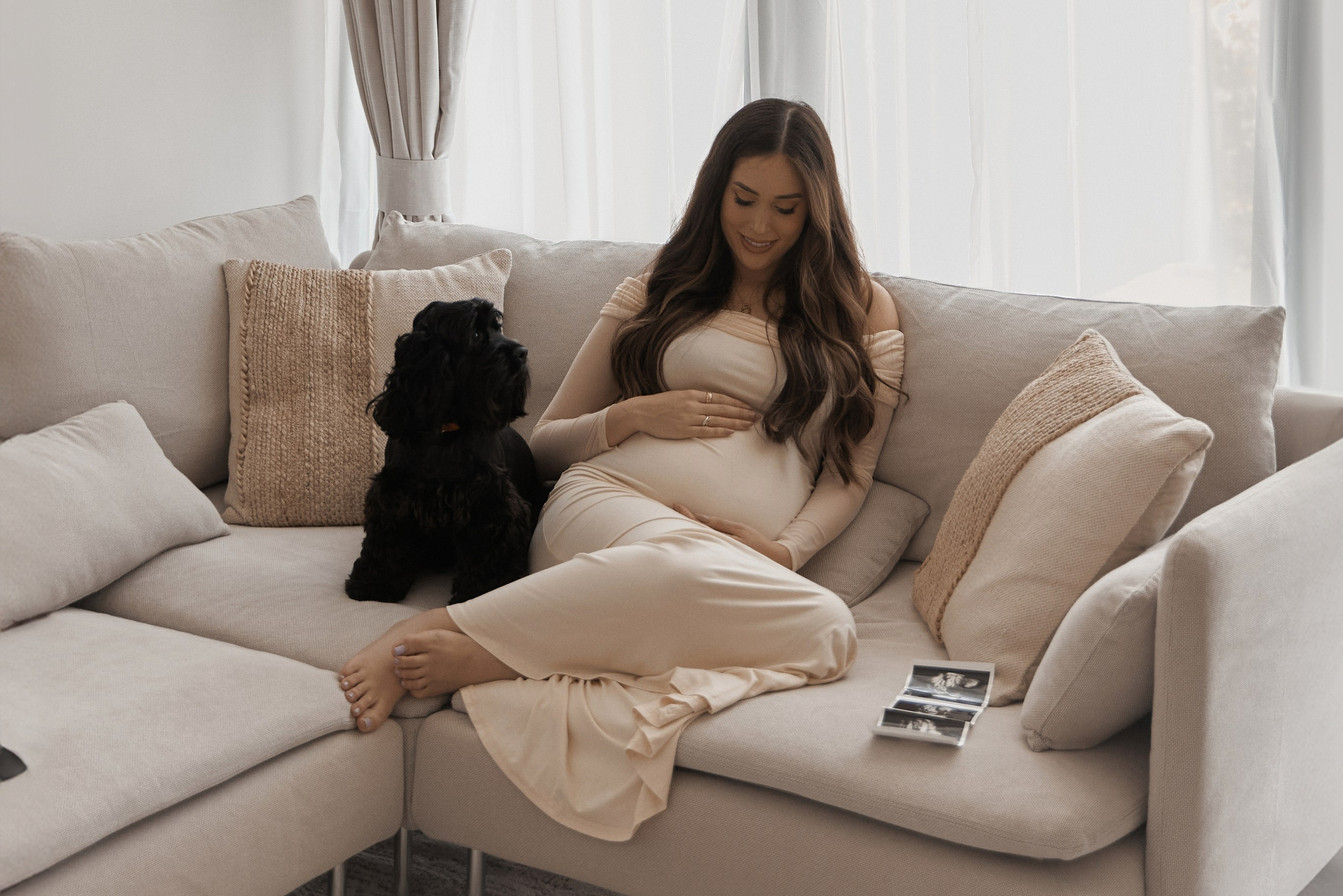 A pregnant woman sitting on a sofa with a dog, showcasing the beauty of pregnancy photography in a cozy living room setting