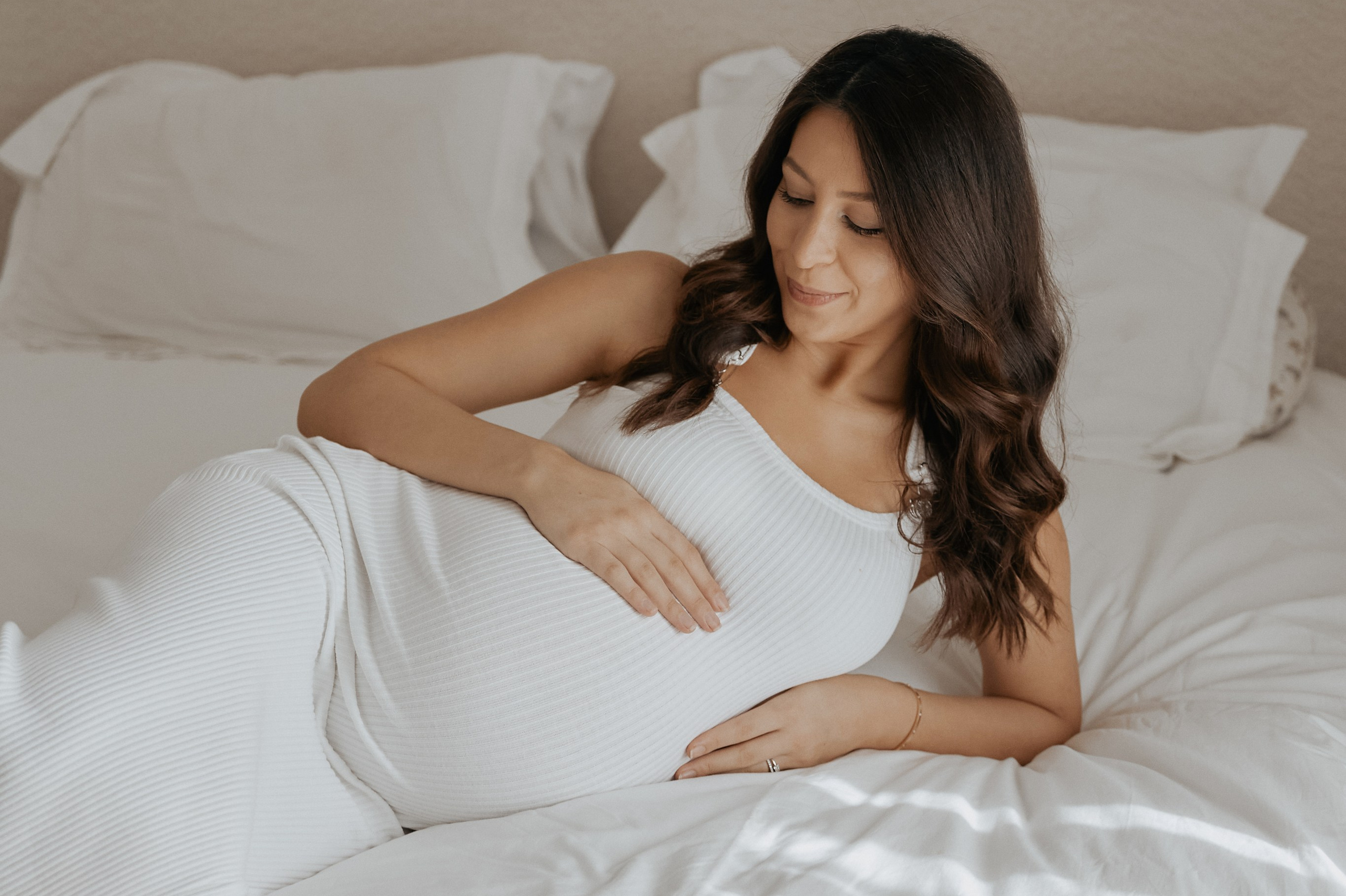 Expectant mother resting on a bed, gently cradling her baby bump during a maternity photoshoot