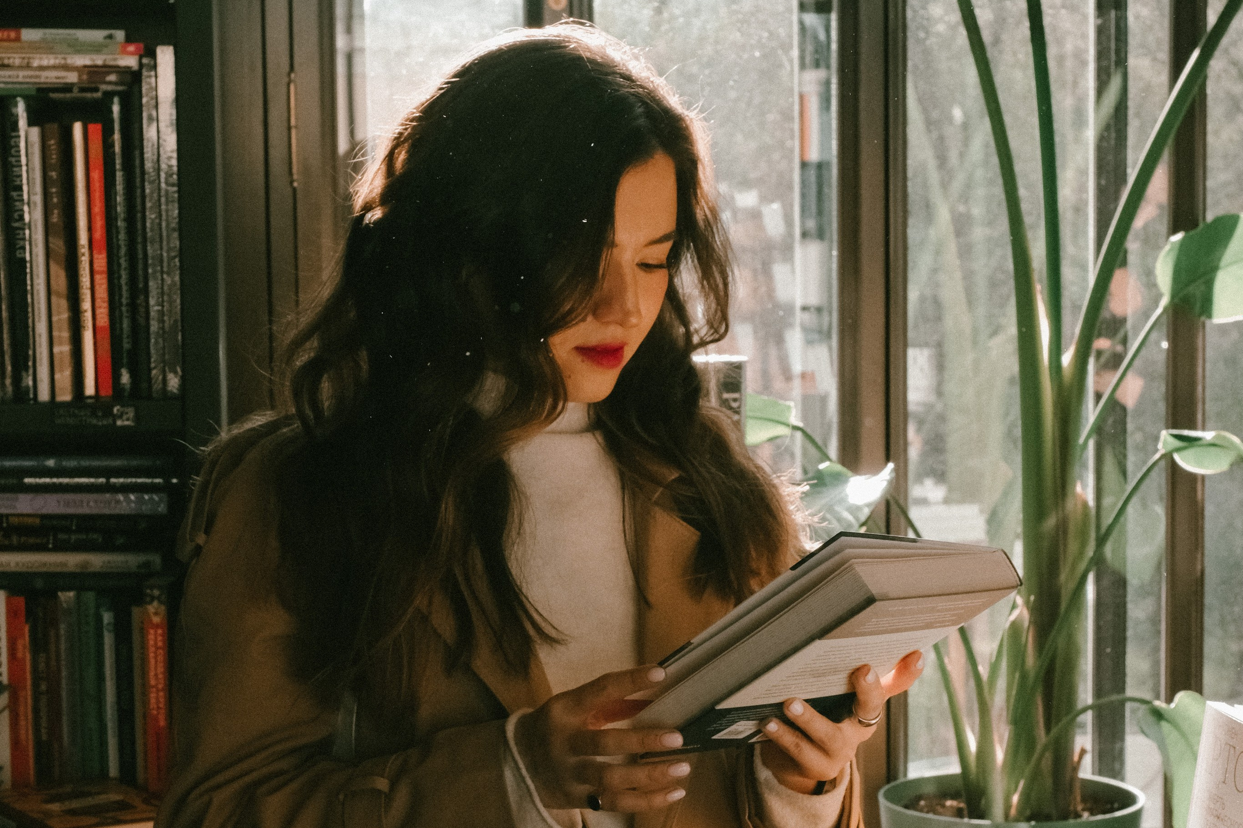 Девушка в тренче и распущенными волосами читает книгу в книжном магазине