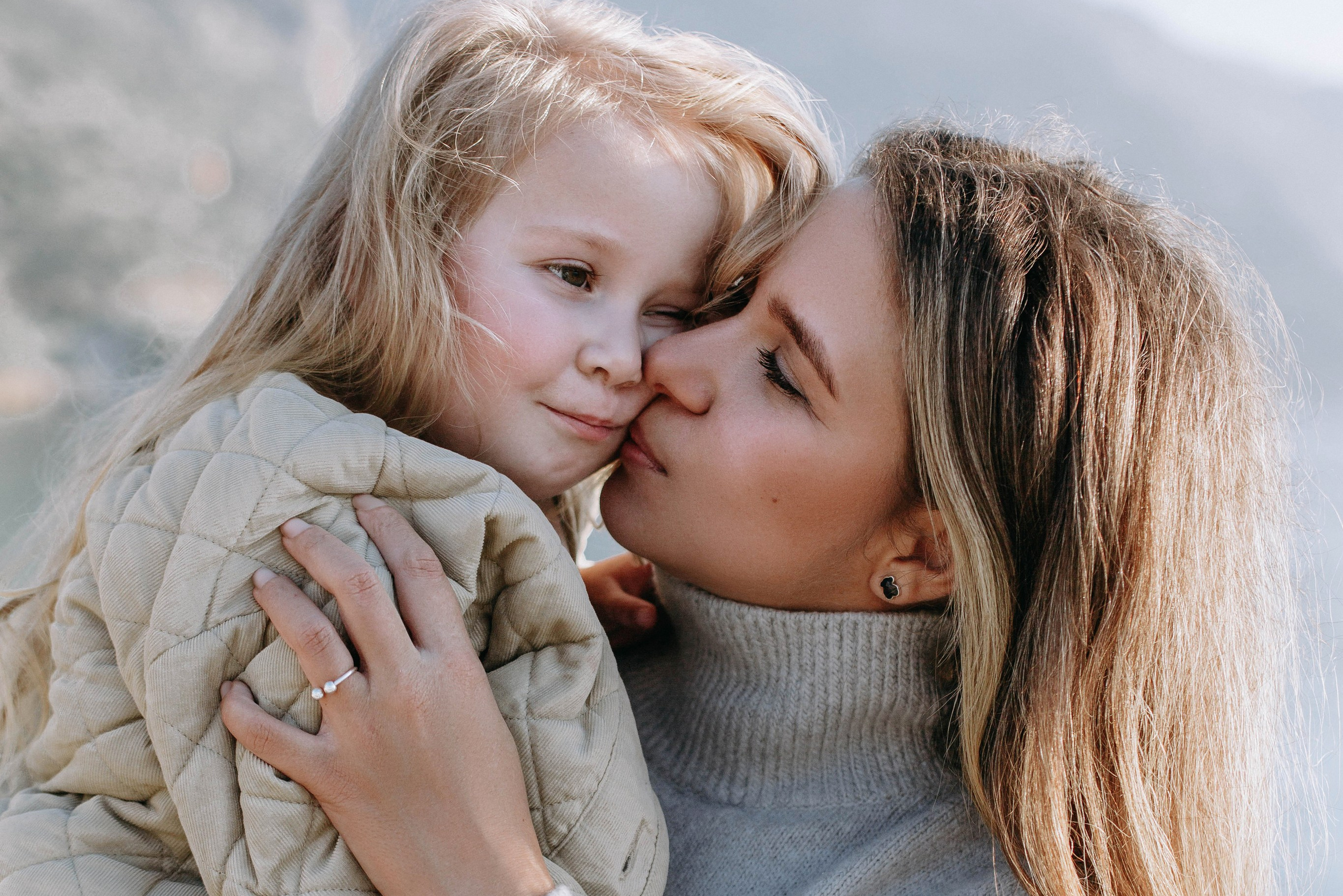 Mother lovingly kissing her young daughter on the cheek outdoors