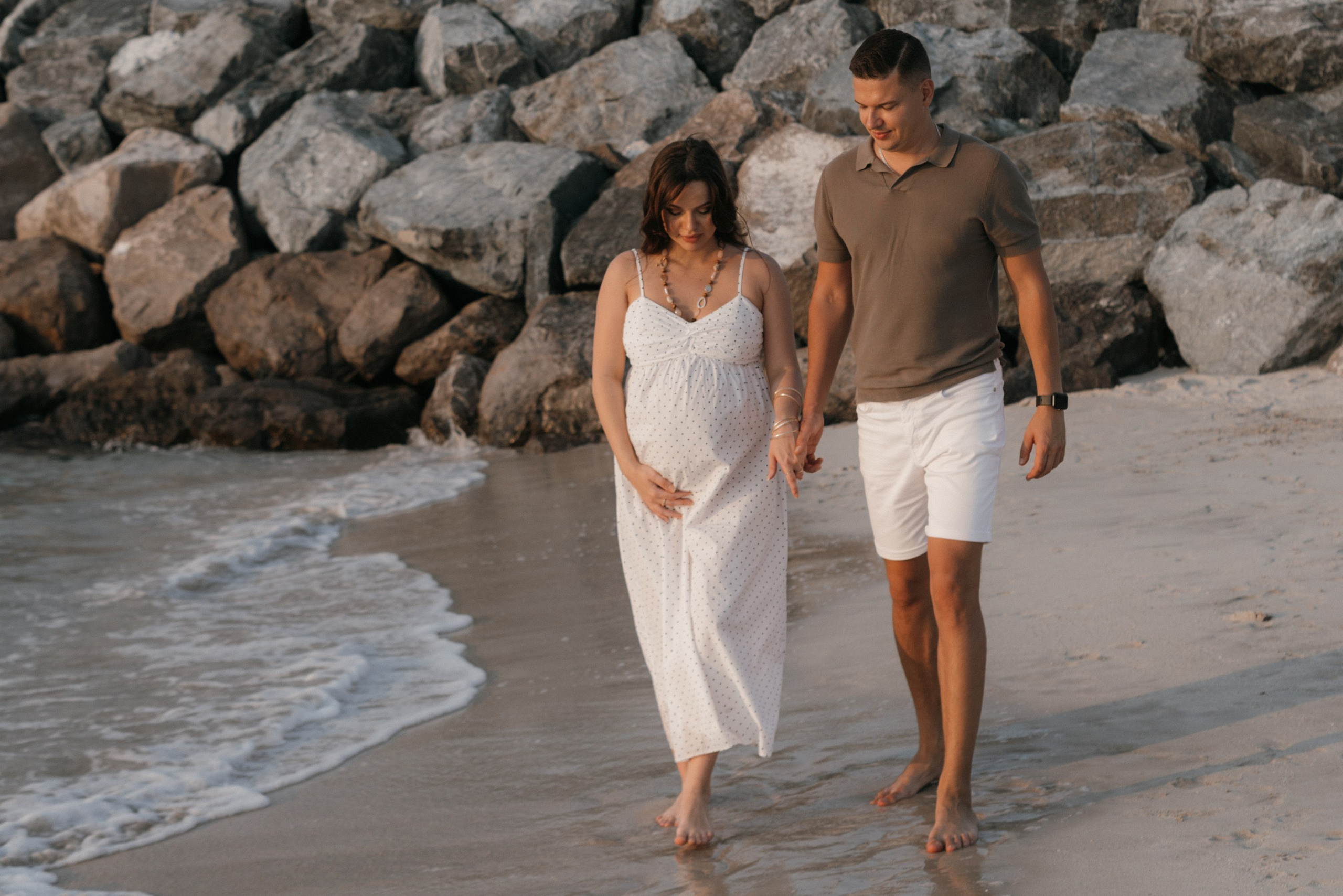 Pregnant woman and man walking together on a beach at sunset