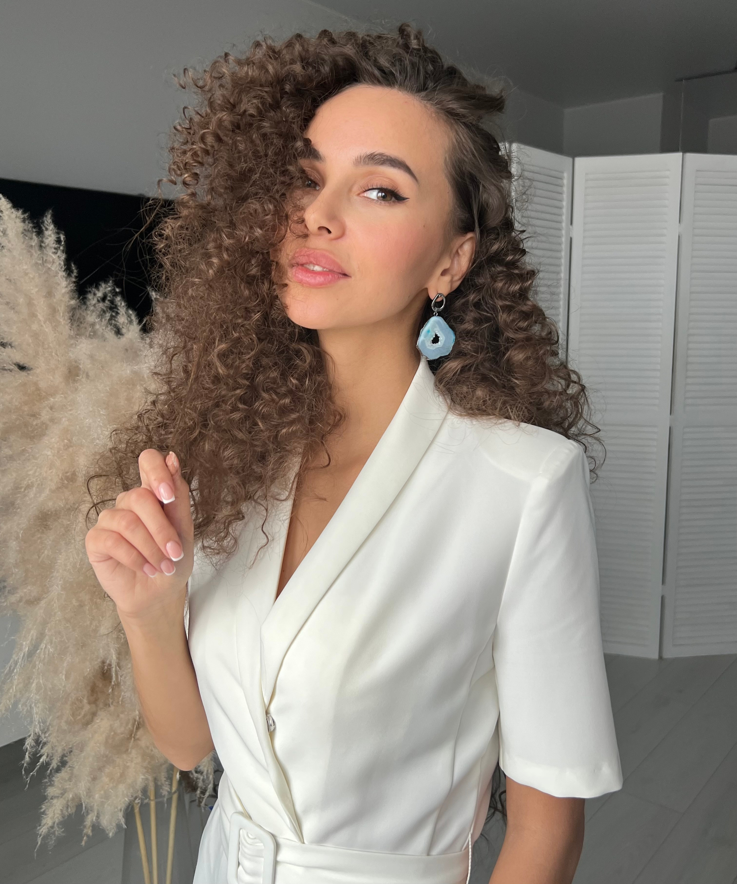 Девушка в голубых серёжках и белом платье стоит смотрит в камеру