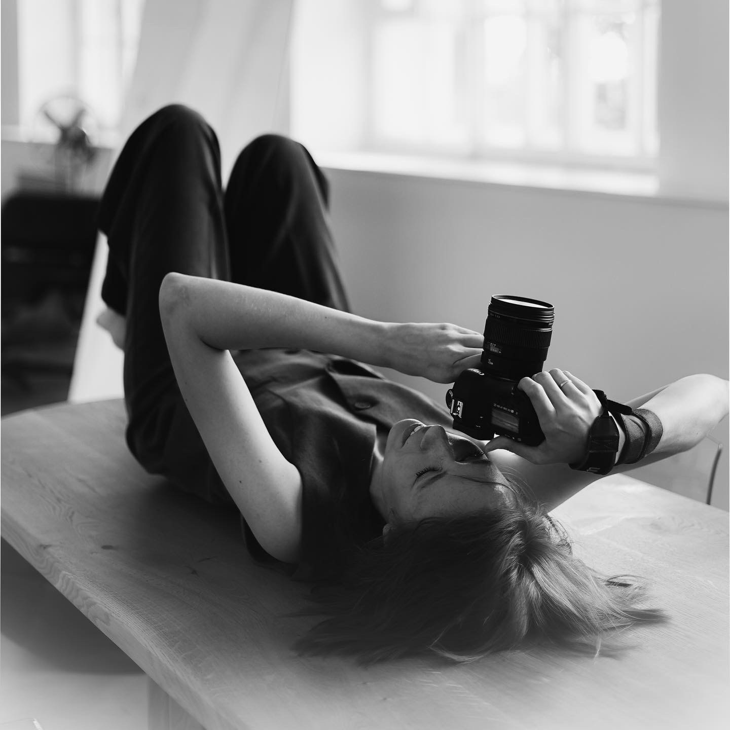 Фотограф девушка лежит на столе с фотоаппаратом и фотографирует лежа.