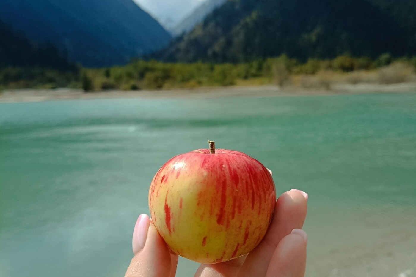 Вид на Лунный Каньон реки Чарын недалеко от Алматы, окружённый зелёными деревьями и кустарниками, на фоне красочных скал в солнечный день. На переднем плане женщина сидит на утёсе и любуется пейзажем