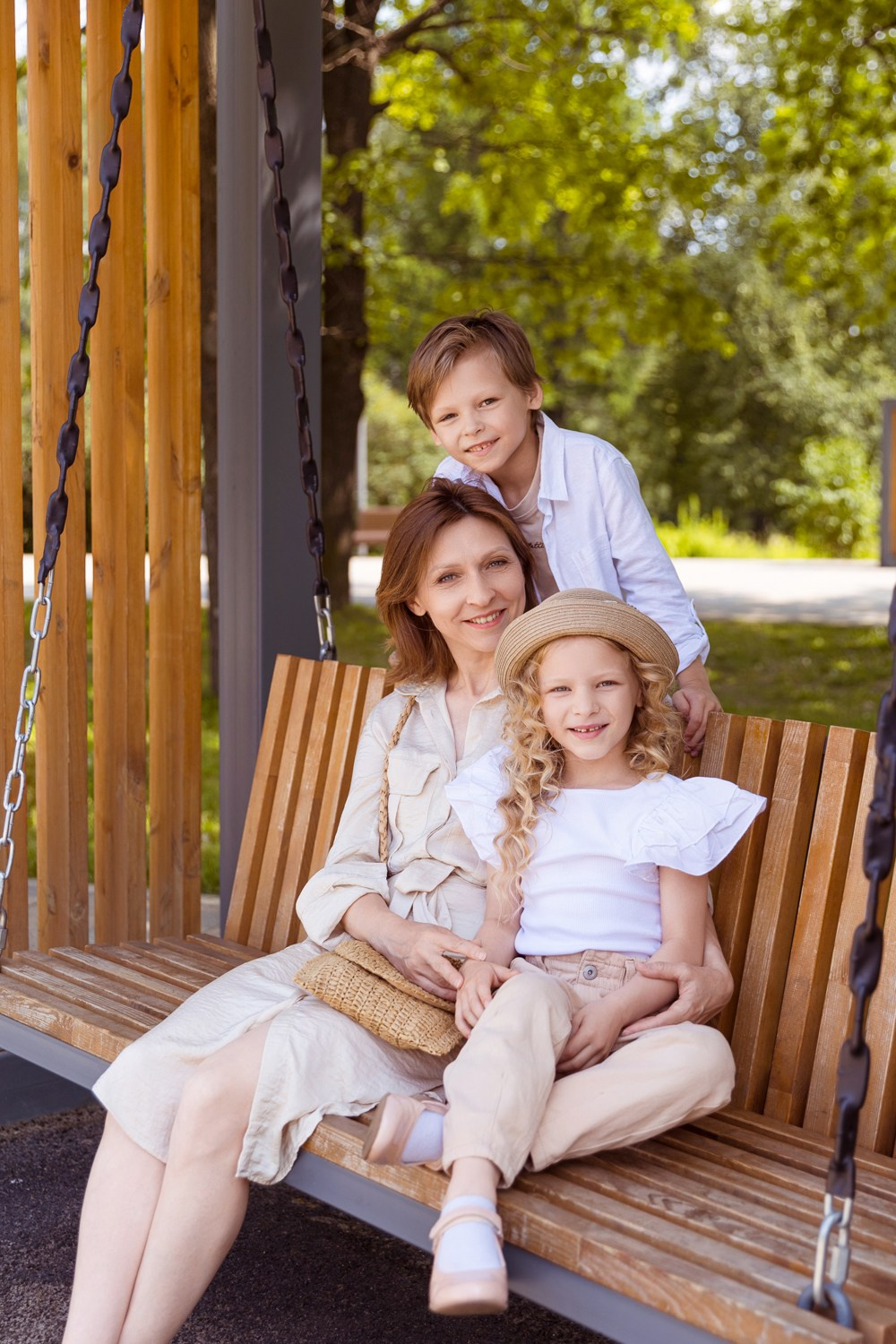 Семья из трёх человек сидят на лавочке в парке