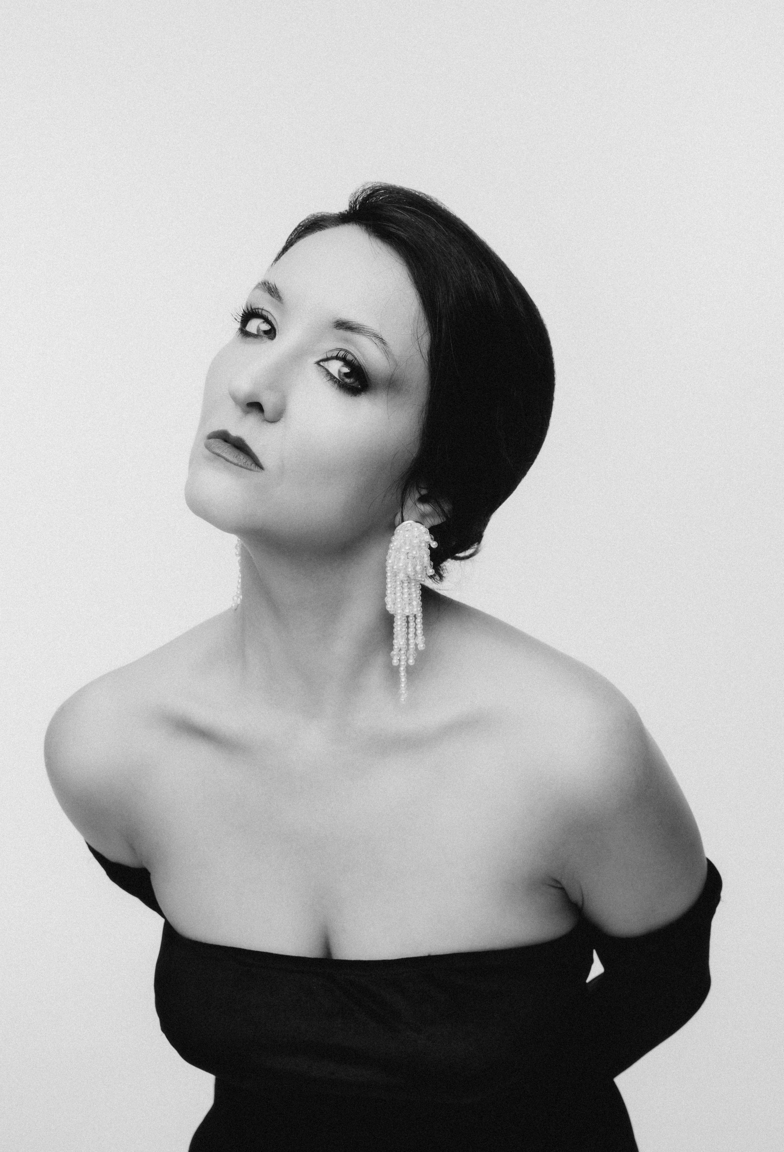 Женщина с жемчужными серьгами прикрывает глаза рукой, экспрессивный черно-белый портрет, Крупный план женщины с выразительным взглядом на камеру, черно-белая художественная фотография.