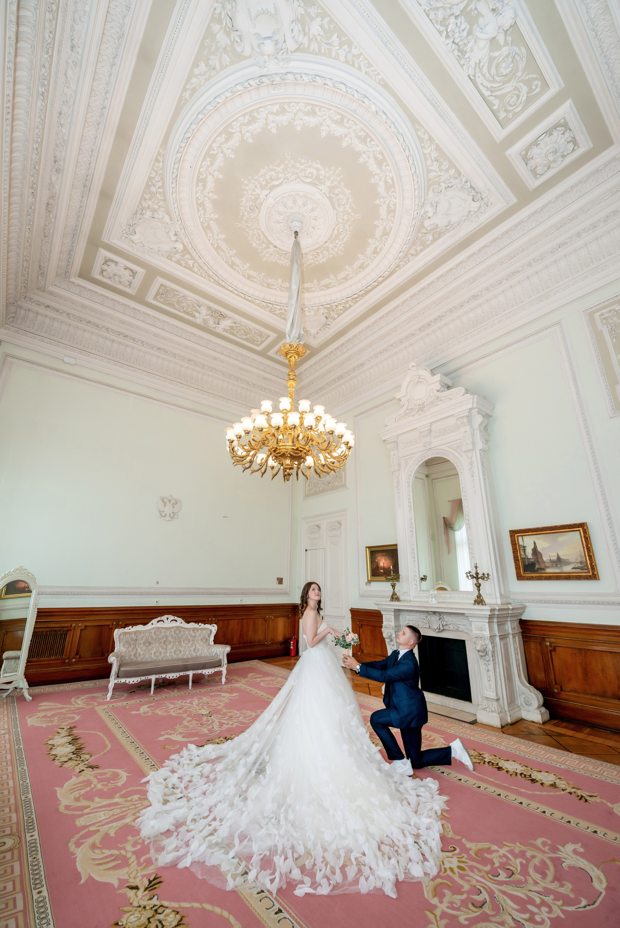 В белом каминном зале жених стоит на колене и делает предложение невесте