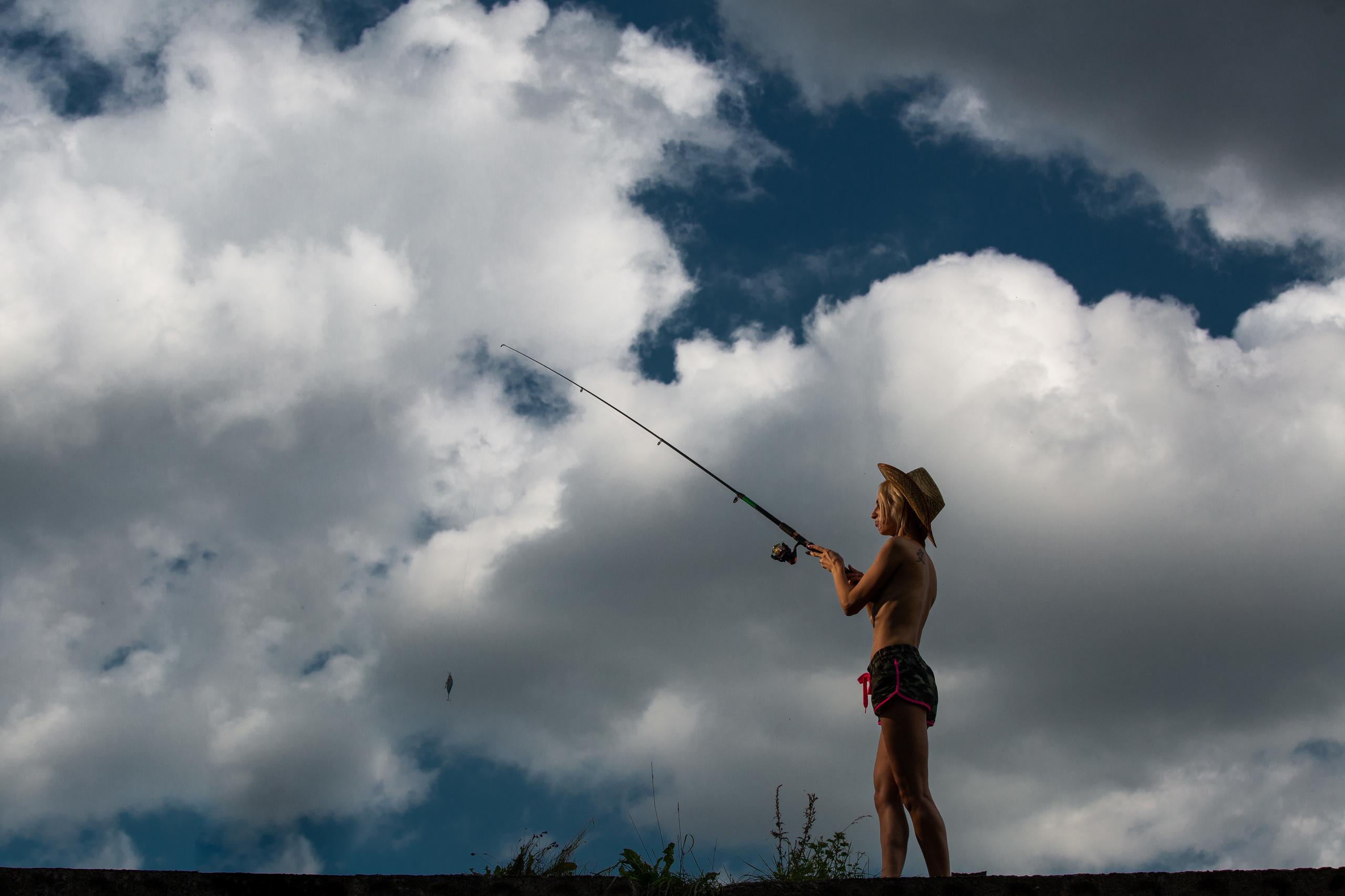 девушка в шортах и с удочкой на фоне неба