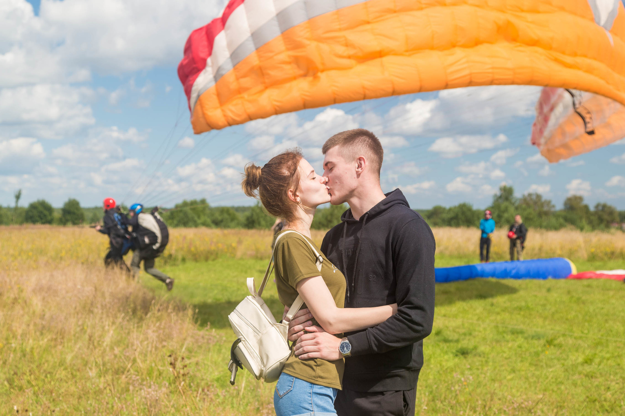 Молодая пара целуется на фоне купола параплана