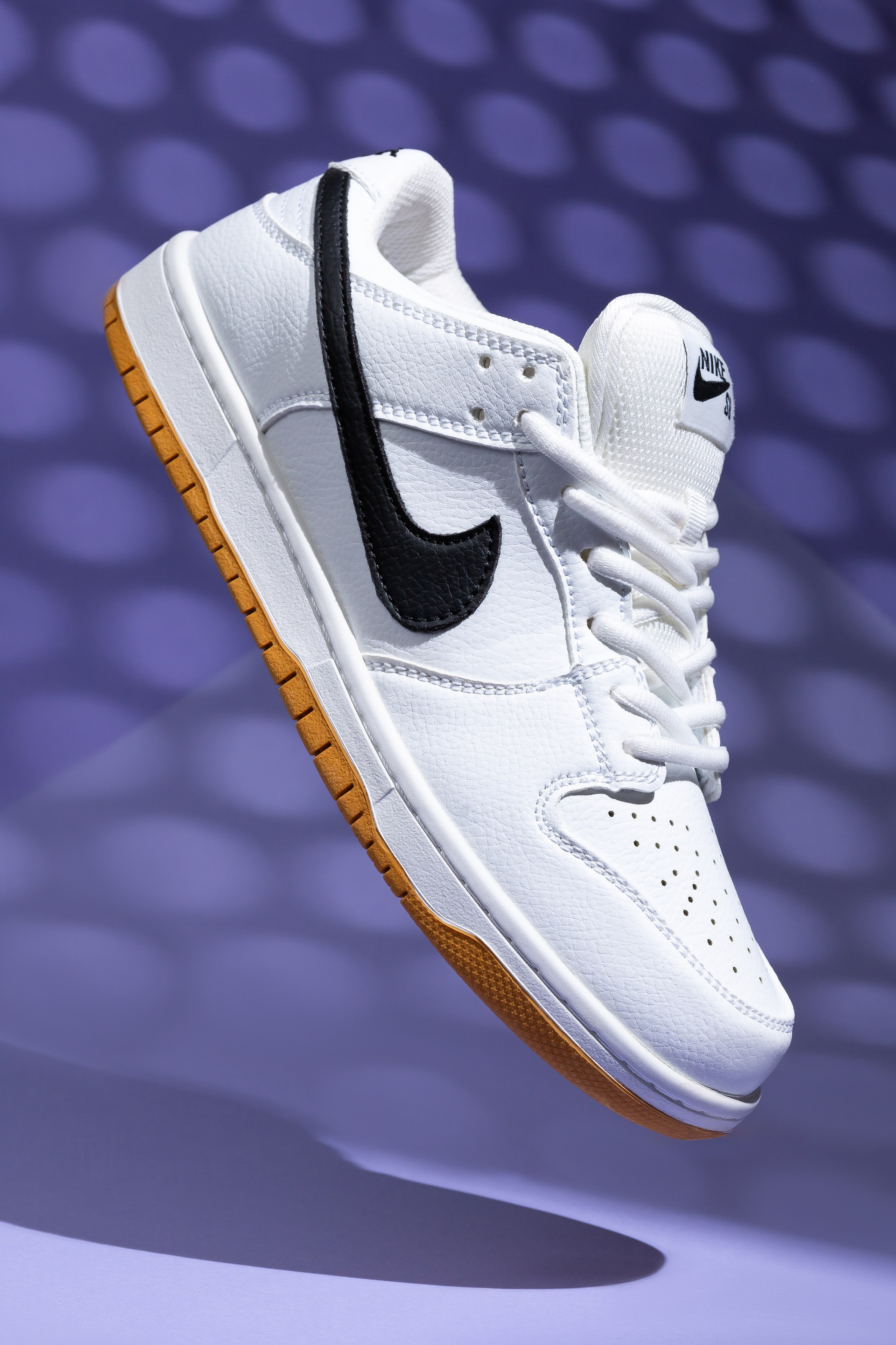 Фотография левитирующего белого кроссовка на фиолетовом фоне