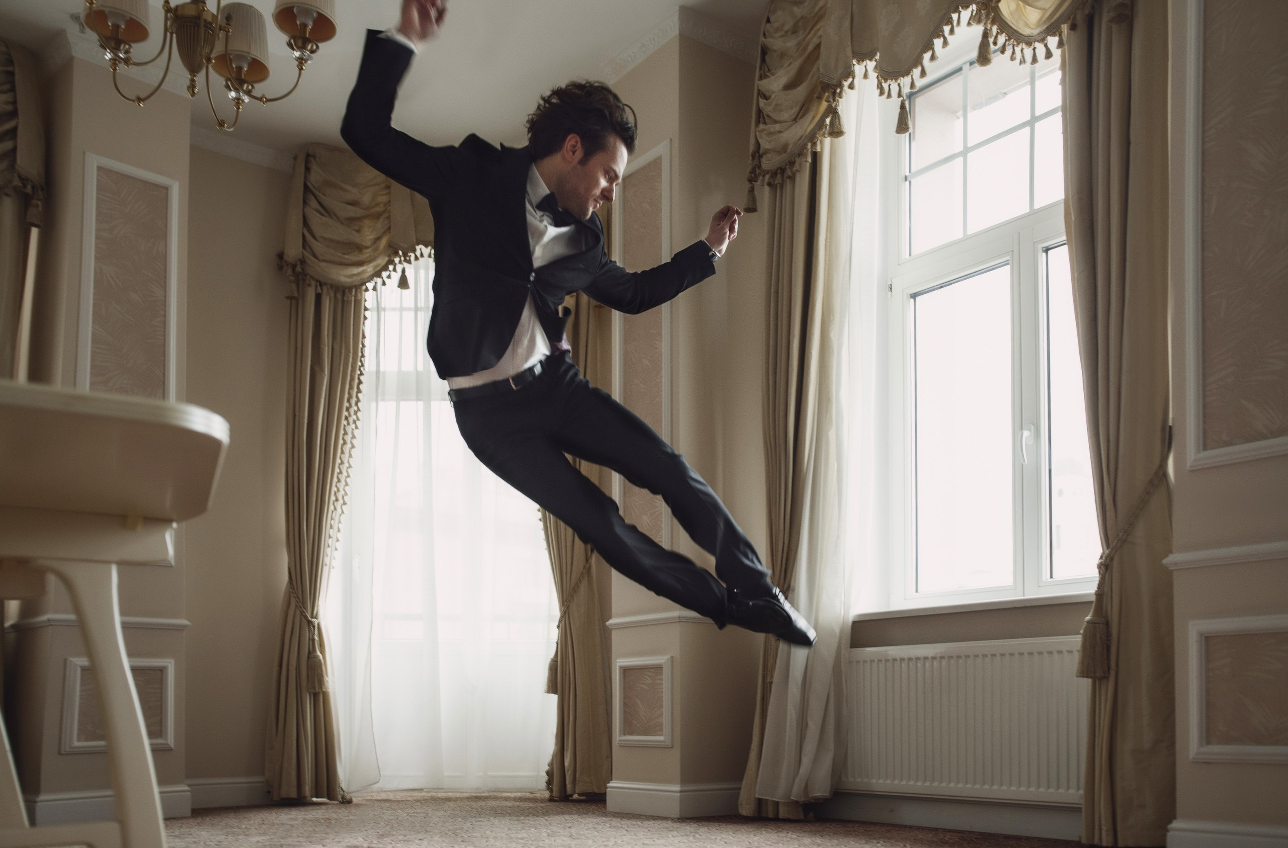 Жених в черном костюме от радости прыгает в номере отеля Европа, Минск. 