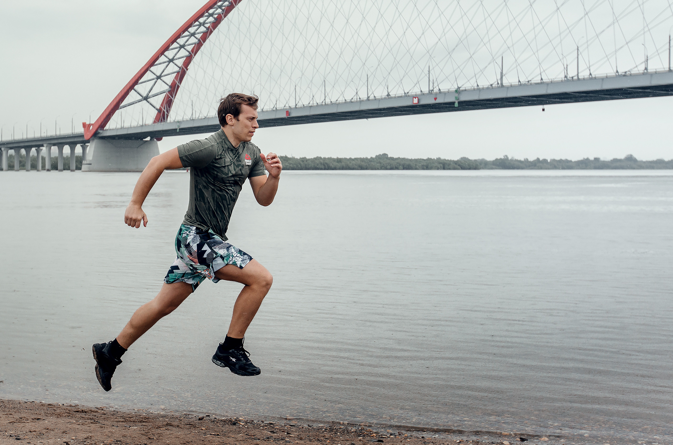 Спортсмен бежит под дождем на фоне воды